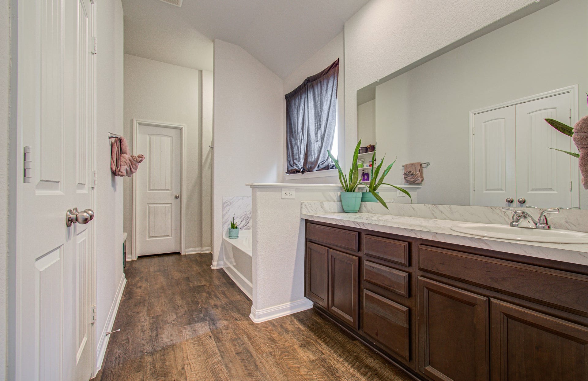 11064 Patriot Court, Cleveland, TX 77328 Spacious primary bathroom featuring elegant dark wood cabinetry, sleek marble countertops, and rich wood-like flooring, accented by a large mirror and abundant natural light.