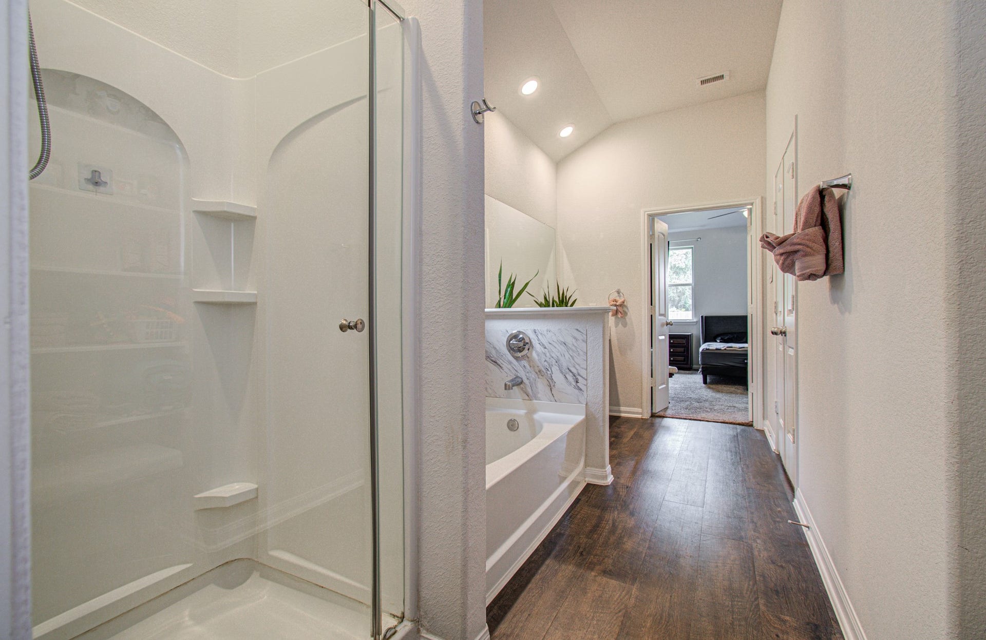 11064 Patriot Court, Cleveland, TX 77328 Elegant primary bathroom featuring a spacious walk-in shower, luxurious soaking tub, and stylish wood flooring, leading to a cozy bedroom.