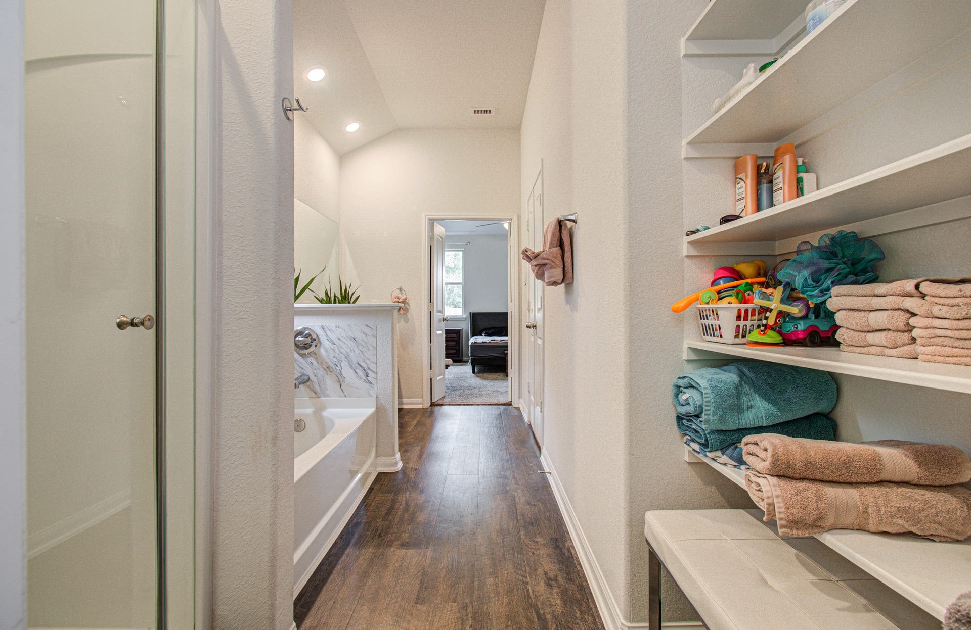 11064 Patriot Court, Cleveland, TX 77328 Bright and inviting primary bathroom featuring a modern shower, a luxurious bathtub, and ample shelving for storage, leading into a cozy bedroom.
