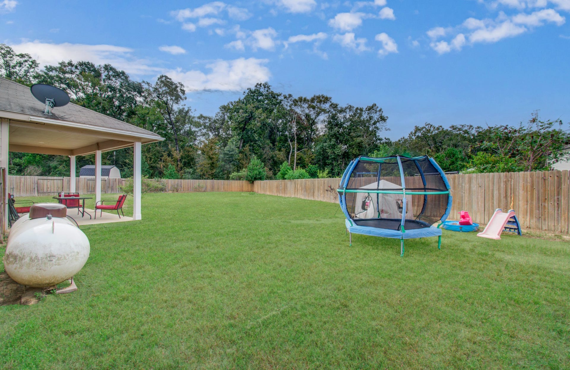 11064 Patriot Court, Cleveland, TX 77328 Expansive backyard featuring a covered patio, perfect for outdoor dining, and ample space for recreation with a trampoline and children's slide.