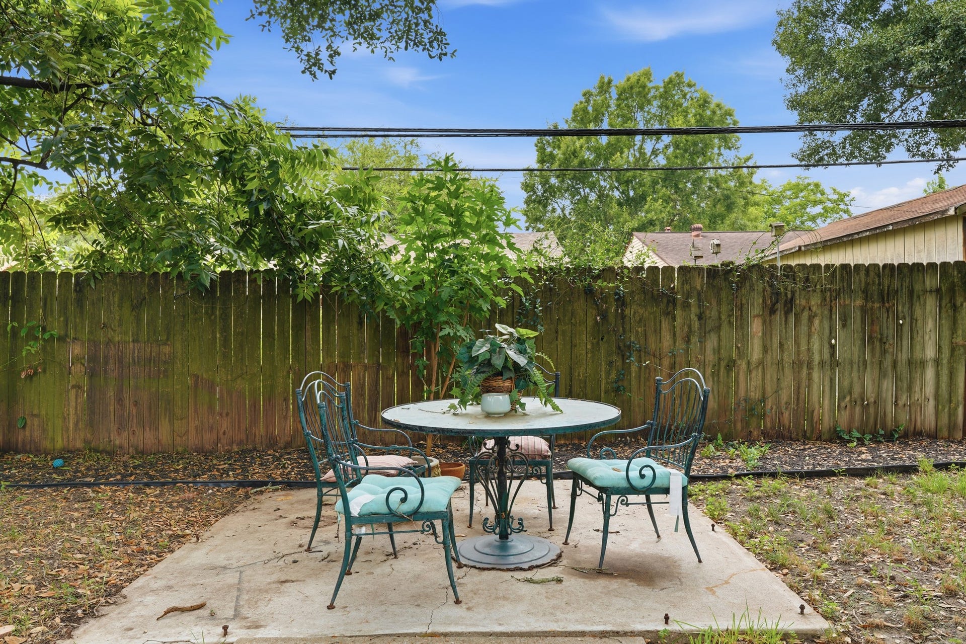 2216 Peach Lane, Pasadena, TX 77502 This outdoor space features a cozy patio with a round table and four chairs, perfect for relaxing or entertaining. It's set on a concrete slab and surrounded by a wooden fence with lush greenery, providing a sense of privacy and tranquility.