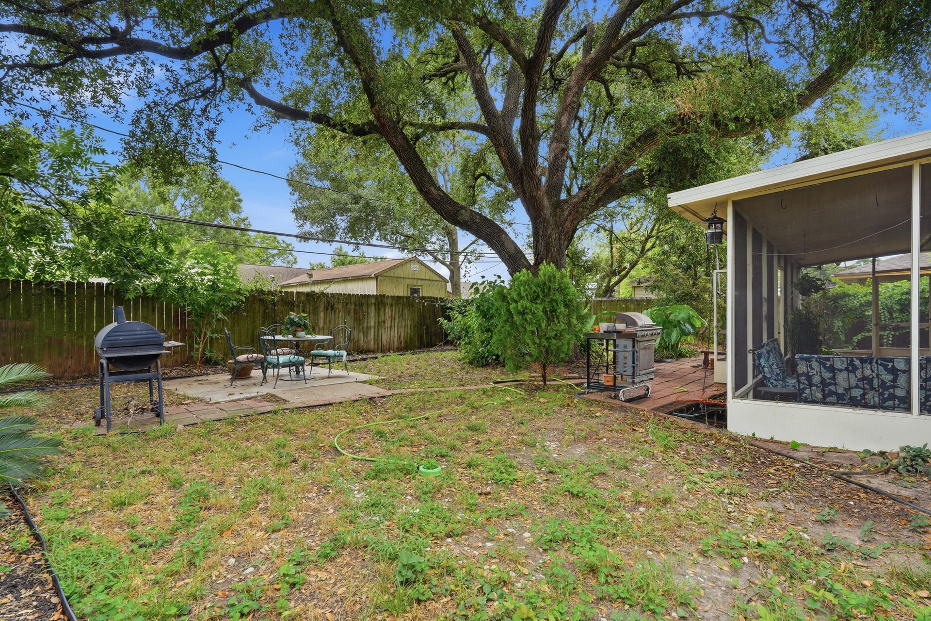 2216 Peach Lane, Pasadena, TX 77502 This backyard features a spacious, shaded area with a large tree, screened porch, and outdoor seating. It includes a grill for entertaining and is enclosed by a wooden fence for privacy.