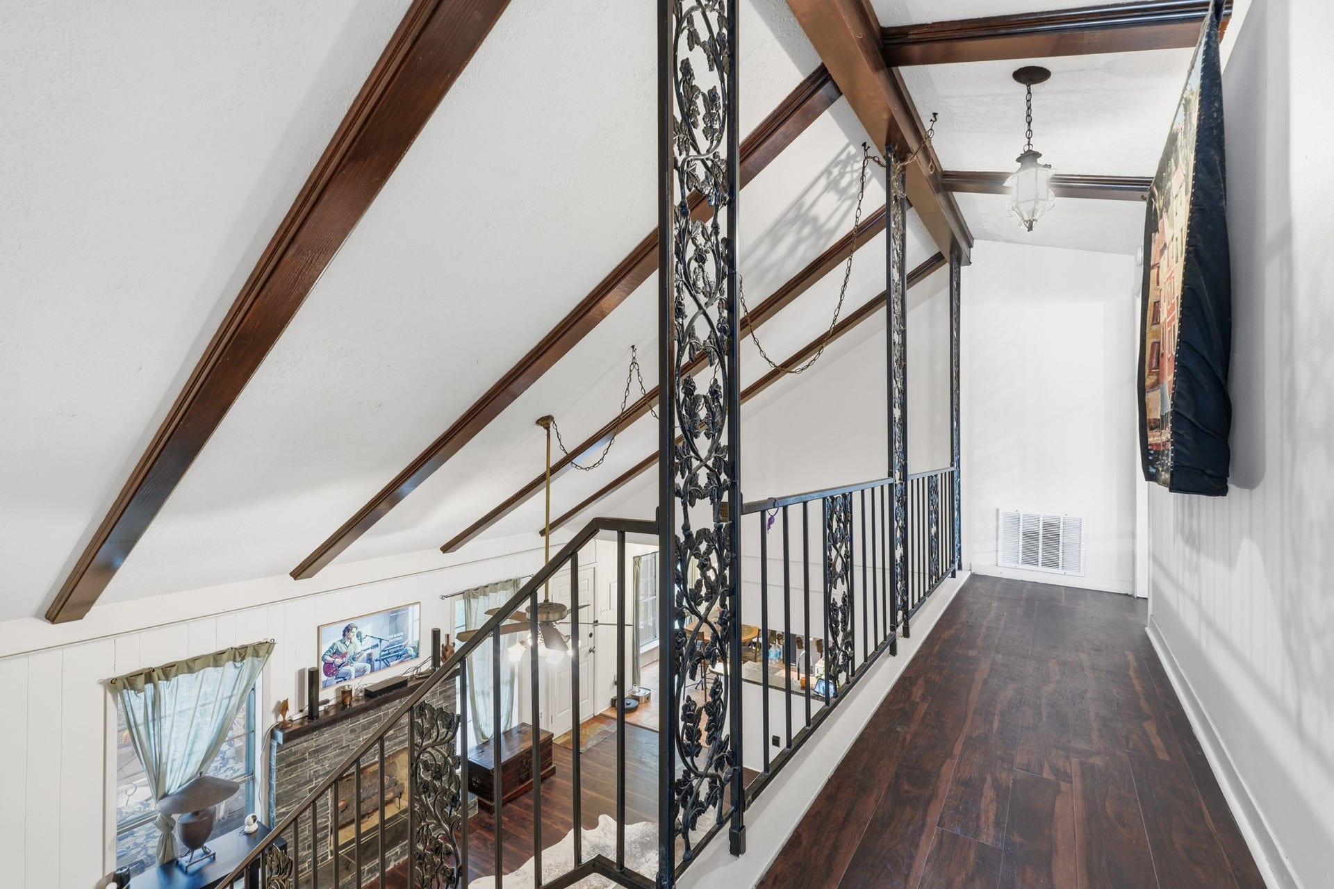 2216 Peach Lane, Pasadena, TX 77502 This photo showcases a stylish loft area with dark wooden floors and elegant wrought-iron railings. The space features vaulted ceilings with exposed wood beams, enhancing its spaciousness and character. Natural light filters in through the windows, creating a warm and inviting atmosphere.