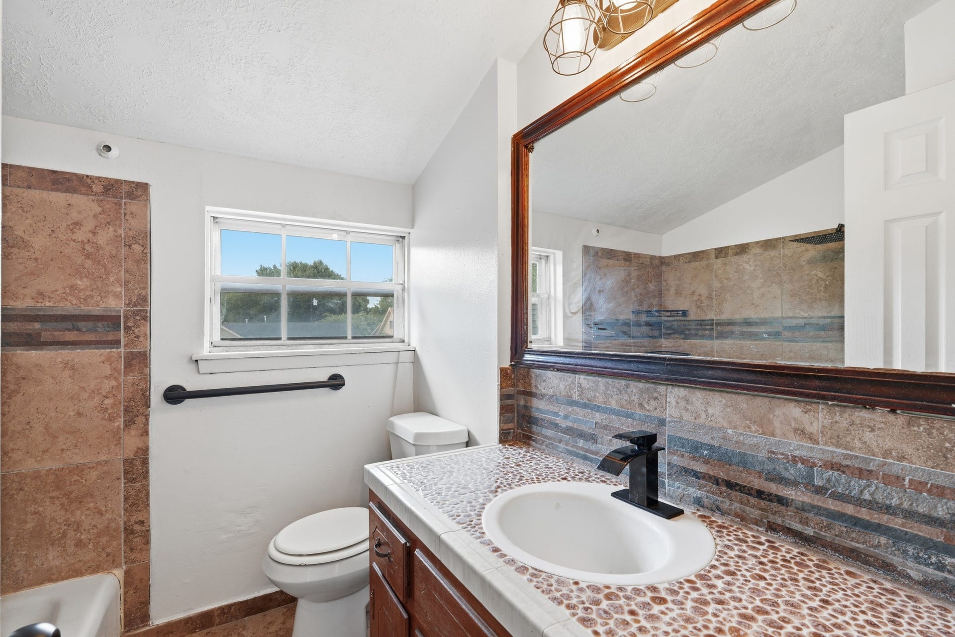 2216 Peach Lane, Pasadena, TX 77502 This charming upstairs bathroom features a rustic design with natural stone accents, a large mirror, and abundant natural light, creating a serene and inviting space.