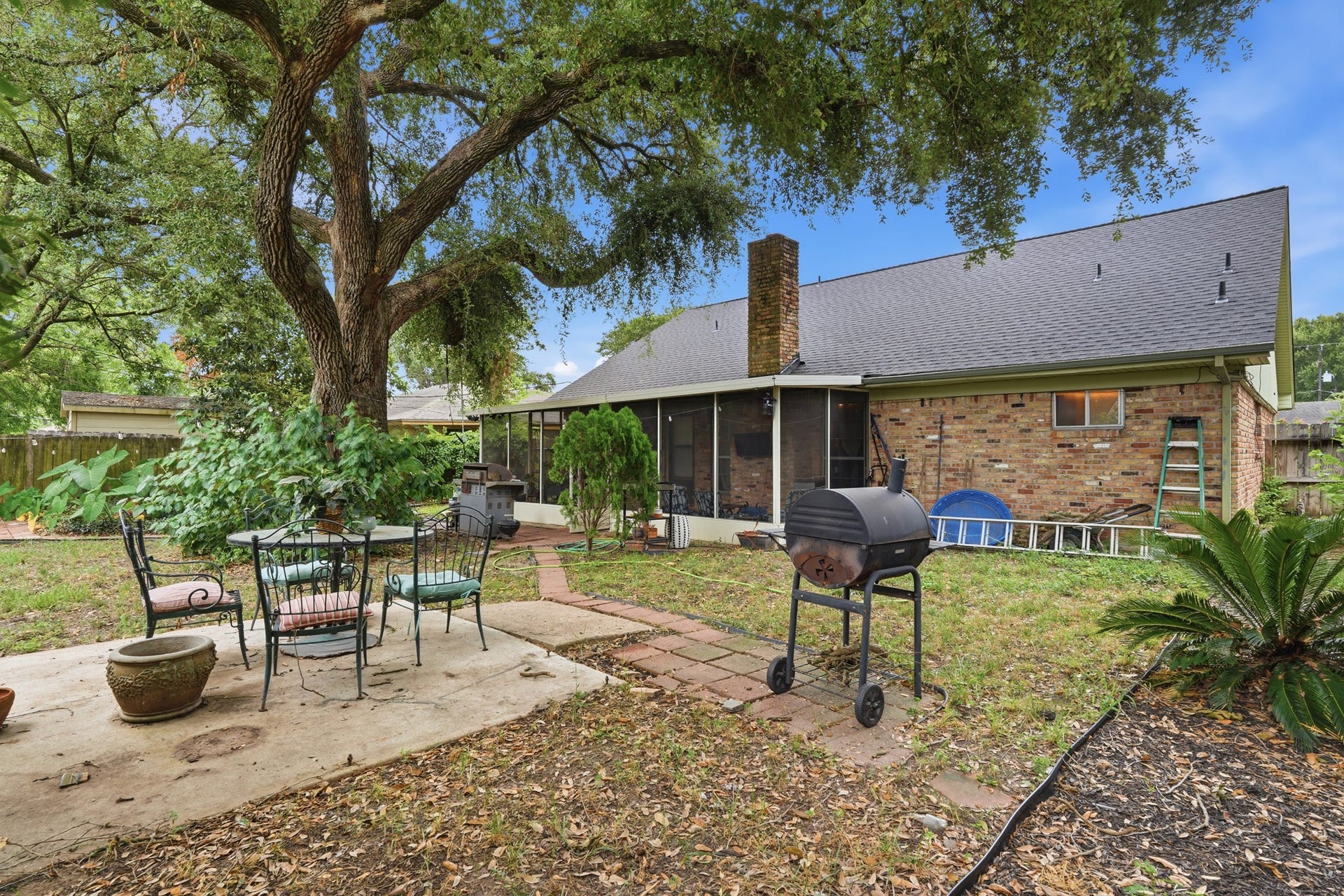 2216 Peach Lane, Pasadena, TX 77502 Charming backyard with mature trees, a patio area for outdoor dining, and a brick house featuring a screened porch. Ideal for relaxation and entertaining.