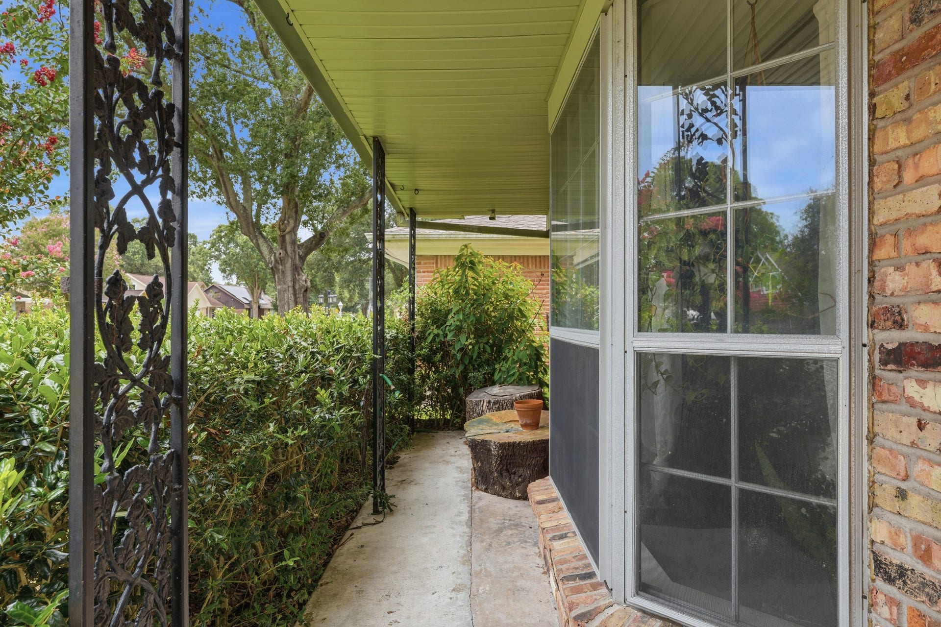 2216 Peach Lane, Pasadena, TX 77502 Step into this charming front porch, where intricate ironwork and lush greenery create a cozy, inviting space perfect for relaxing and enjoying the neighborhood's tranquility.