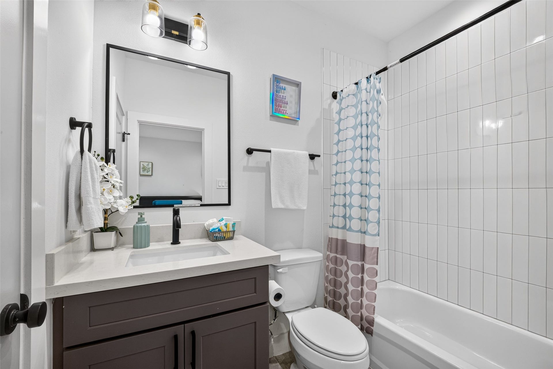 The first bedroom's full bath features a clean vanity setup and a classic shower-tub combination, carrying the home's clean, contemporary aesthetic into the private quarters.