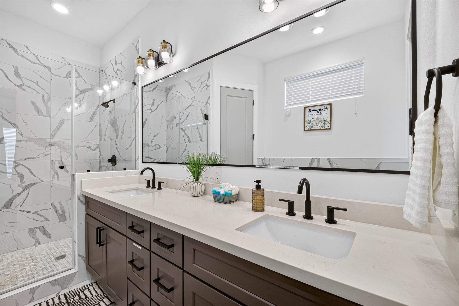 A wide dual-sink vanity stretches beneath an equally expansive mirror, while stylish lighting and a glass-enclosed shower create a polished setting for the start and close of each day.