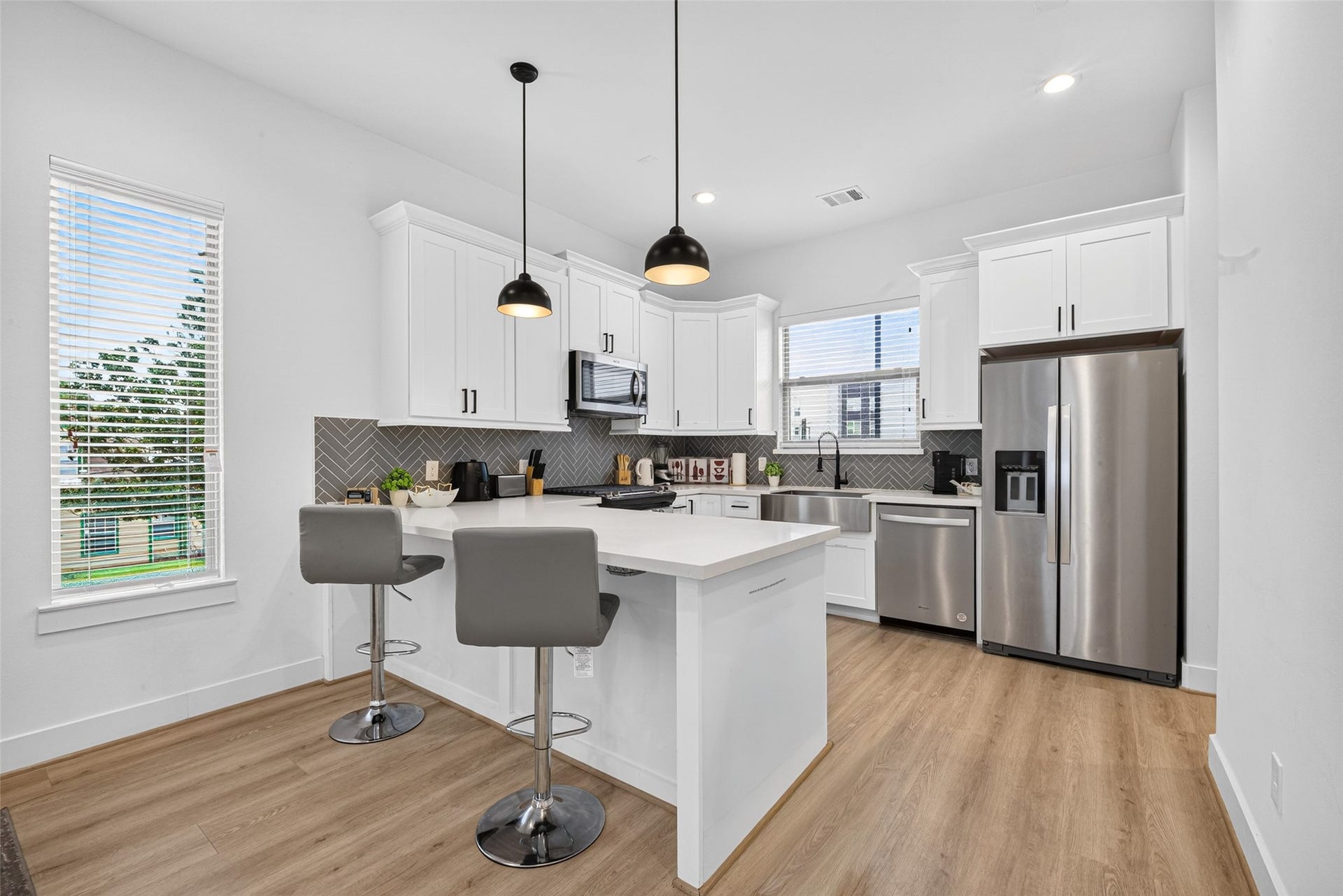 Pendant lights cast a warm glow over the granite breakfast bar, complementing pristine cabinetry and the accentuating backsplash.