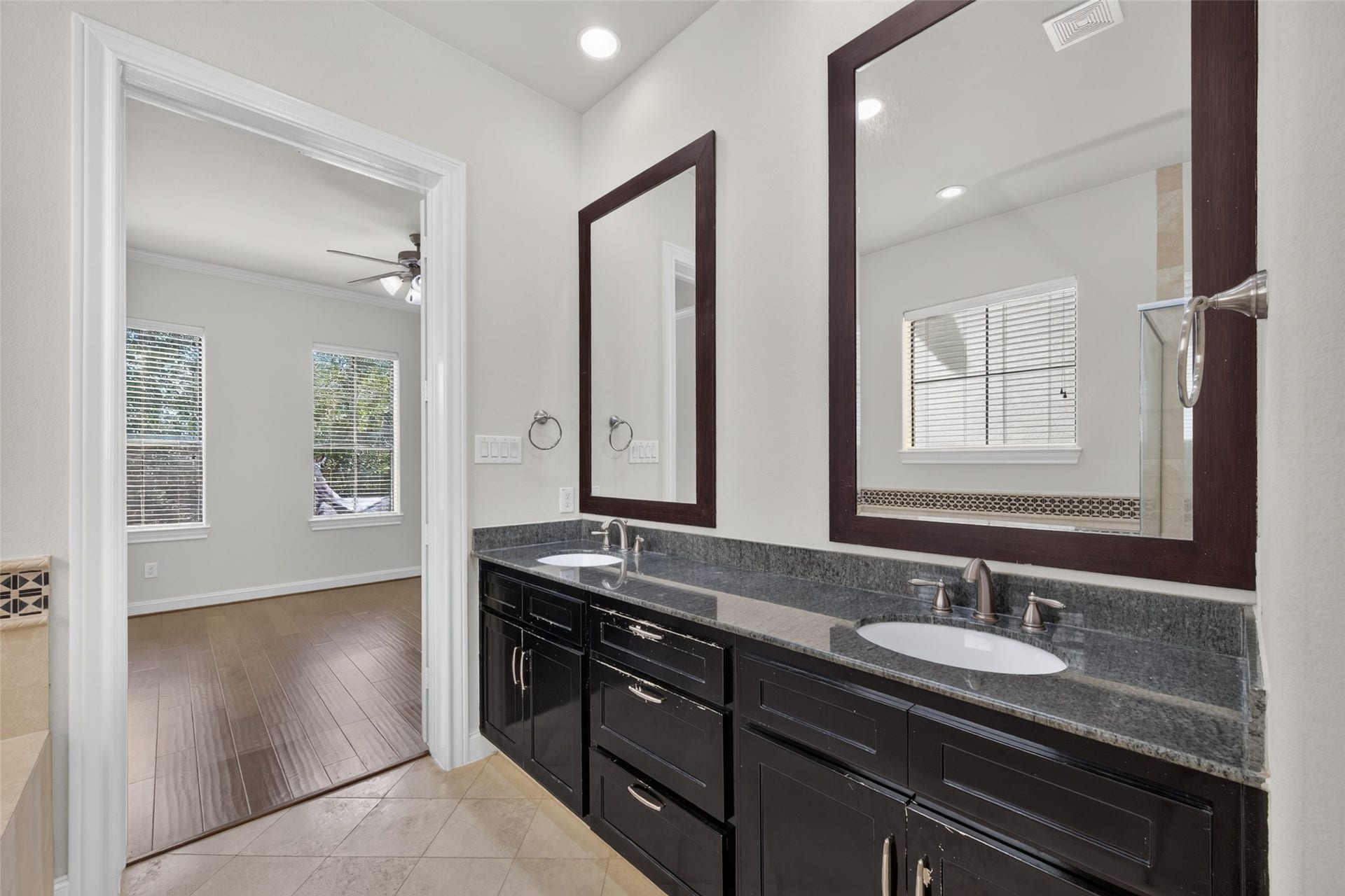 6610 Toledo Street, Houston, TX 77008 Elegant bathroom featuring a dual-sink vanity with dark cabinetry and granite countertops, opening into a bright room with large windows and hardwood floors.