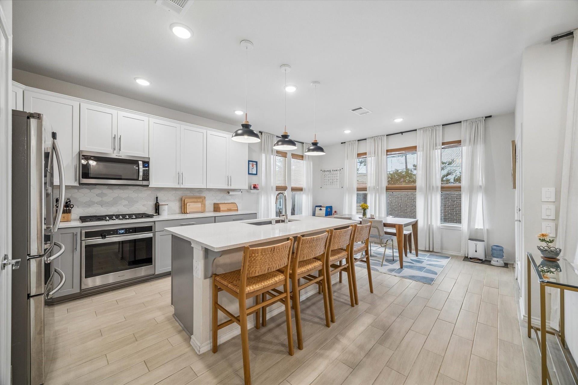 The heart of the home features an oversized island with seating for four, quartz countertops, stainless steel appliances, and a sunlit dining area surrounded by expansive windows.