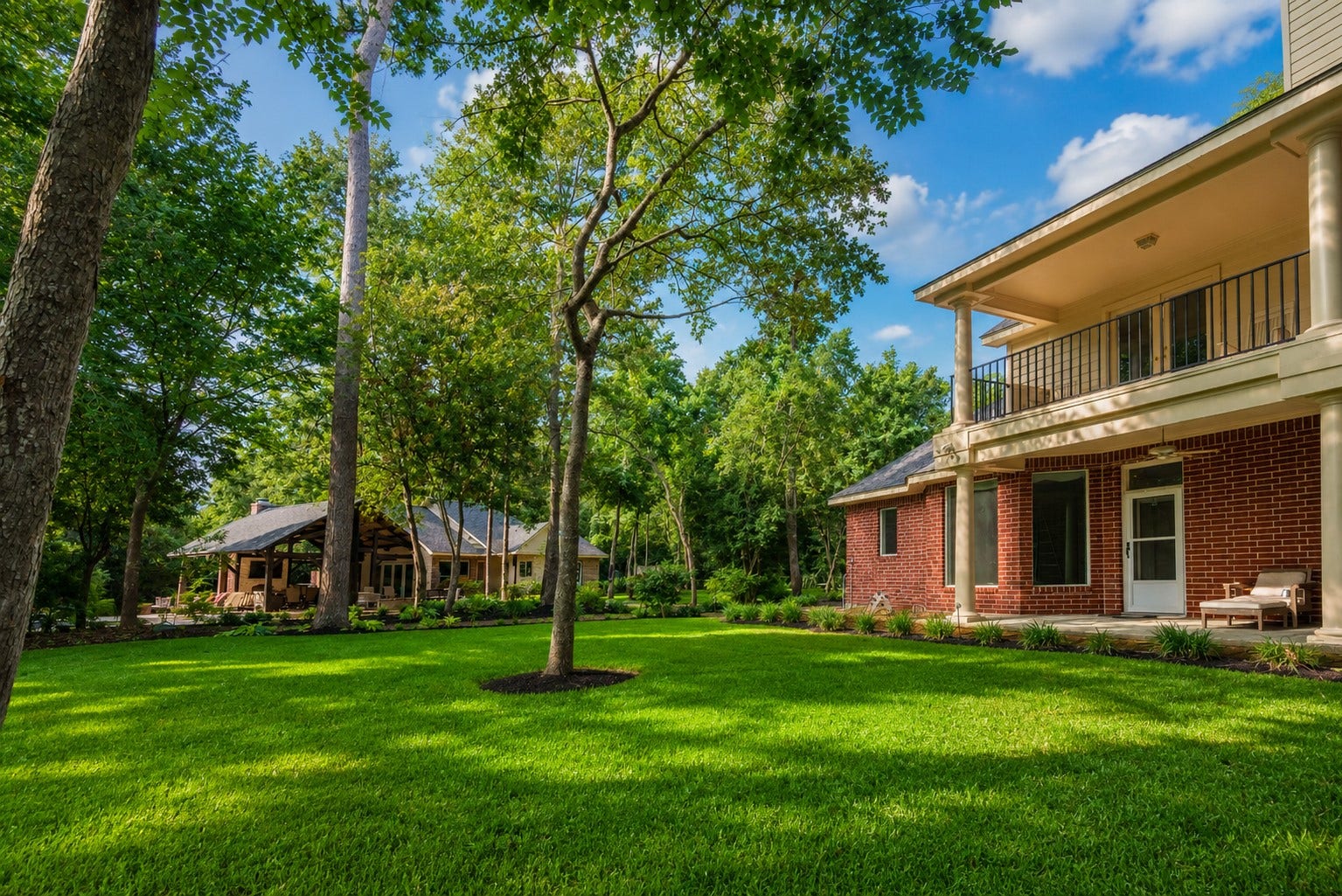 7 Pastoral Pond Circle, The Woodlands, TX 77380 Stunning, lushly landscaped backyard featuring serene views of the main residence, outdoor pavilion, and guest house. This tranquil oasis is perfect for relaxation and entertaining, seamlessly integrating all structures into a cohesive, picturesque living space.