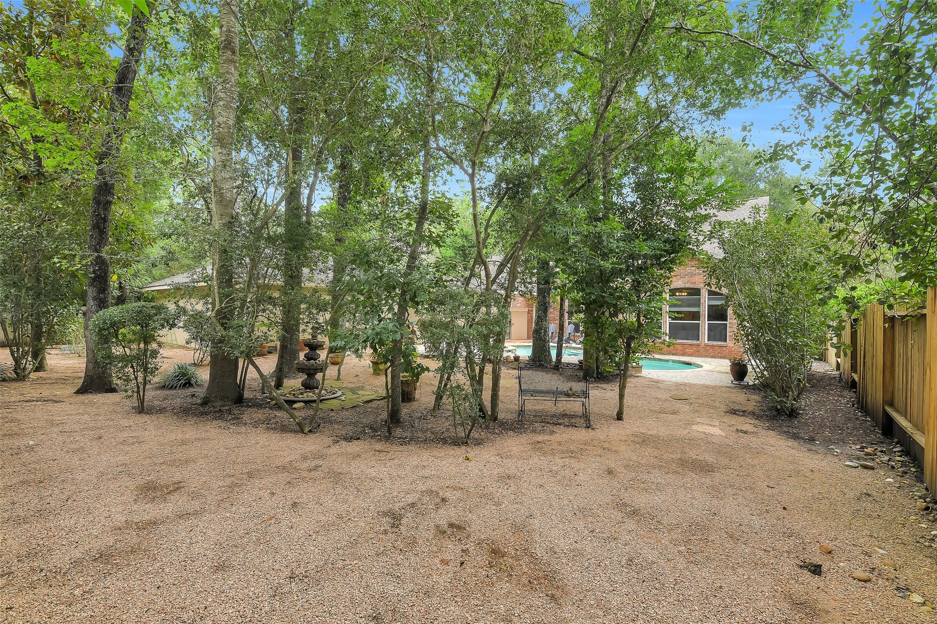 7 Larkspur Trail, The Woodlands, TX 77382 Serene backyard oasis with lush trees, a charming fountain, and a private pool, perfect for relaxation and outdoor enjoyment.