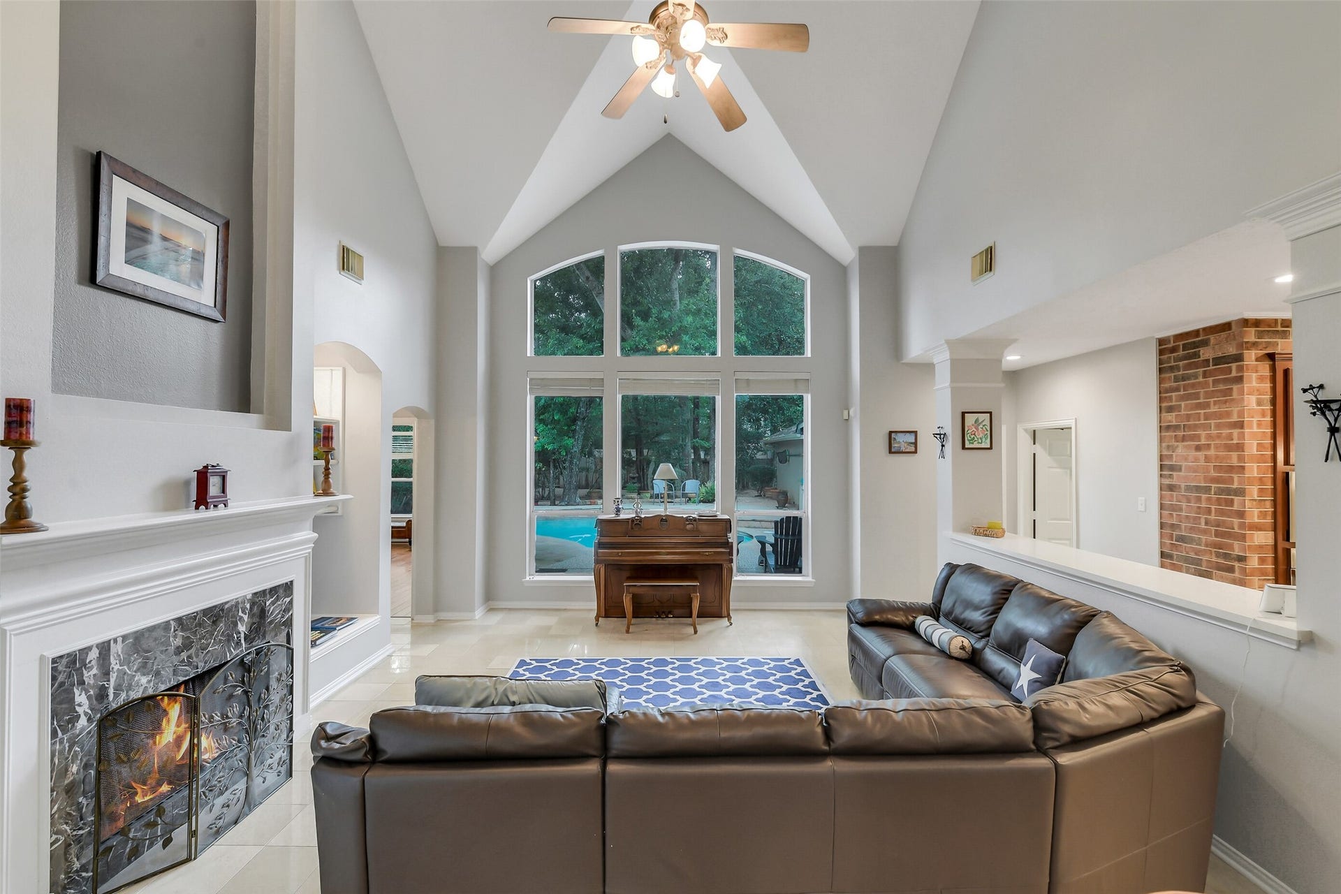7 Larkspur Trail, The Woodlands, TX 77382 Spacious living room with vaulted ceilings, a cozy fireplace, and large arched windows offering serene views of the backyard and pool.