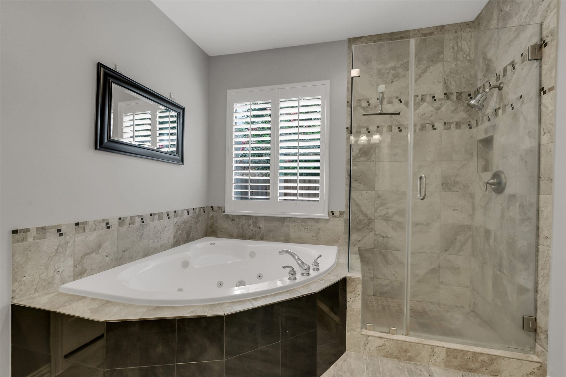 7 Larkspur Trail, The Woodlands, TX 77382 Luxurious Primary bathroom featuring a spacious jetted tub and elegant glass-enclosed shower with stylish tile accents, complemented by a large window with plantation shutters for natural light.