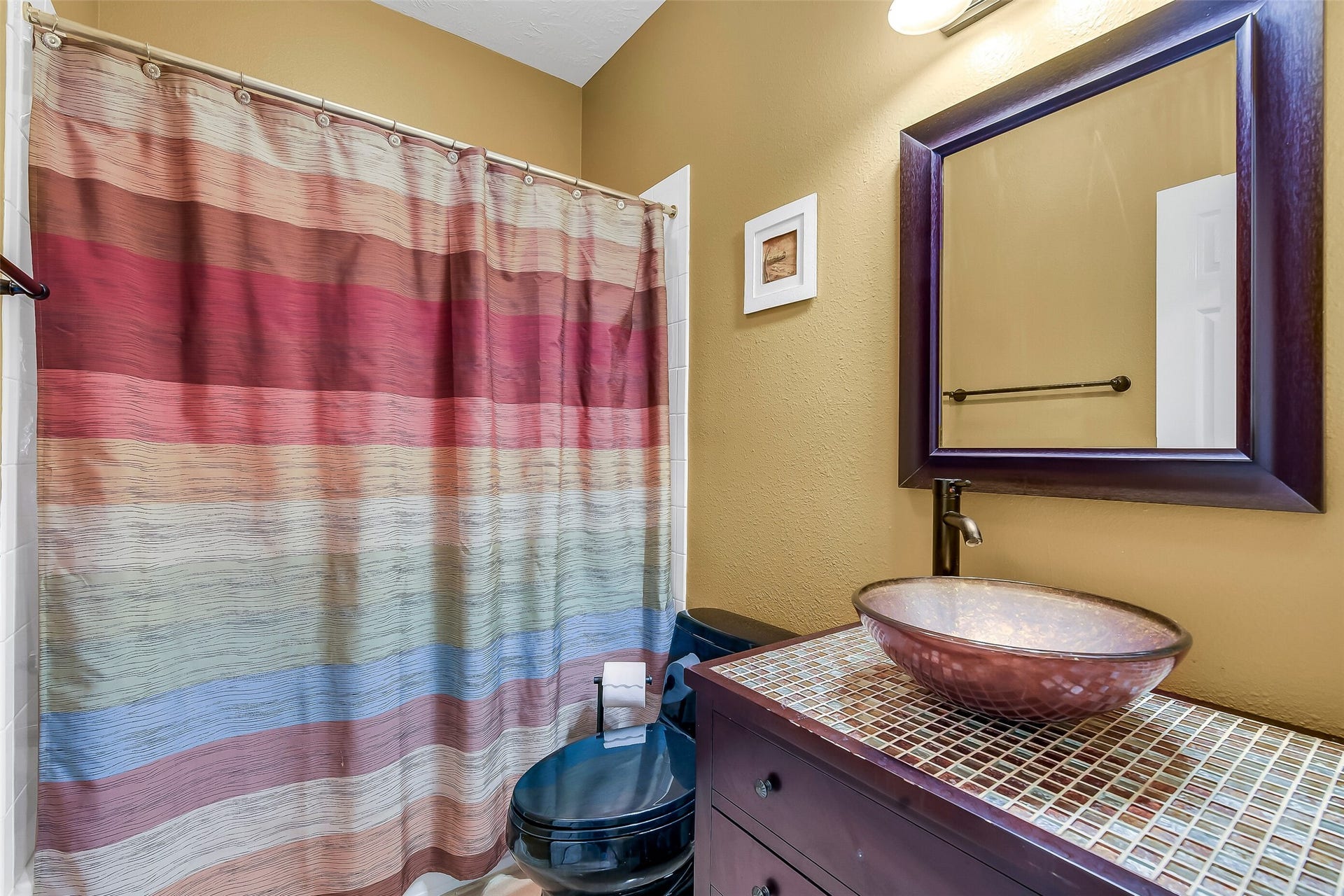 7 Larkspur Trail, The Woodlands, TX 77382 Charming bathroom located near office with a colorful striped shower curtain and a stylish vessel sink atop a tiled vanity, complemented by a warm, earthy wall color.