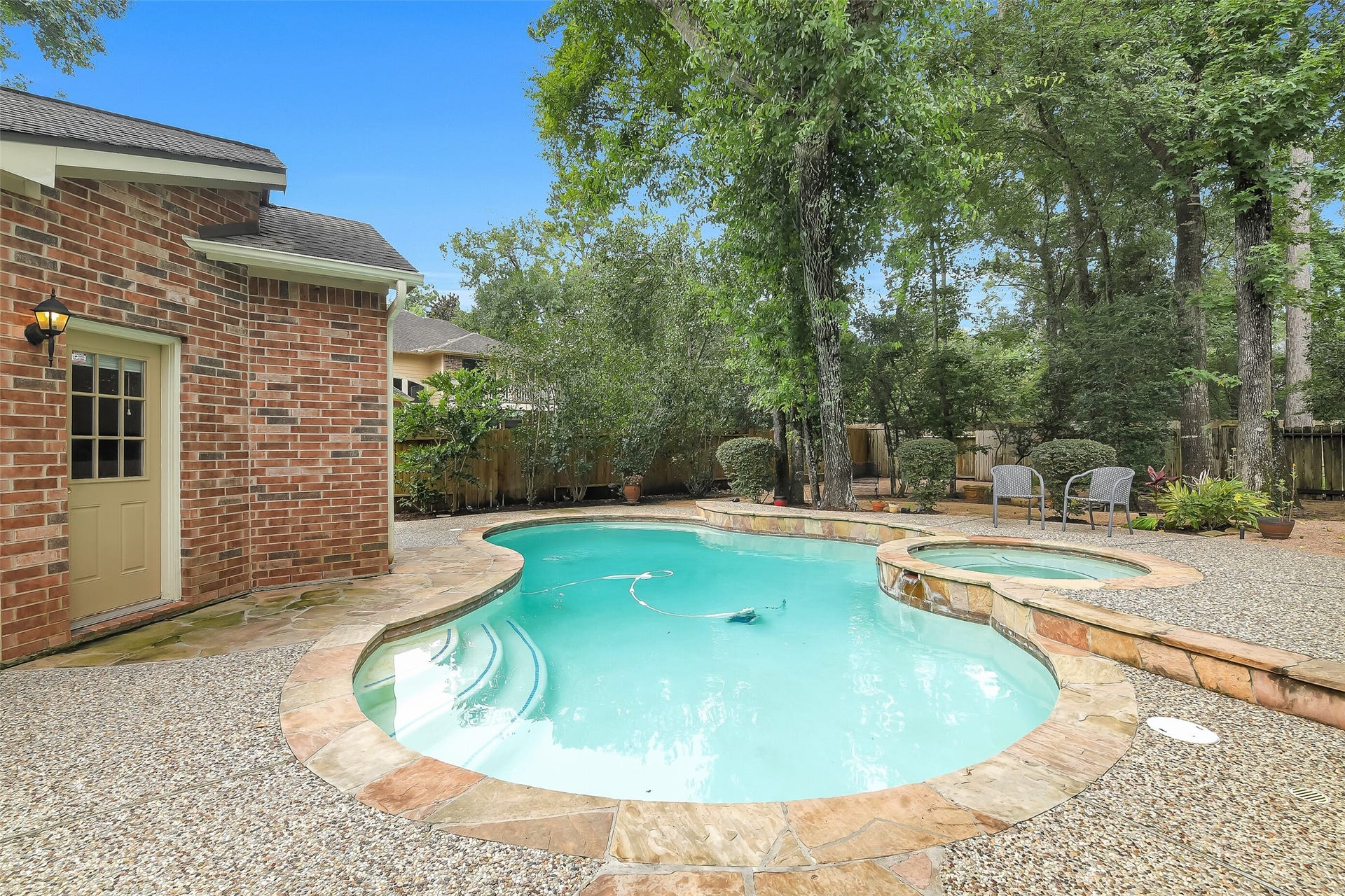 7 Larkspur Trail, The Woodlands, TX 77382 Charming backyard oasis featuring a sparkling pool and spa, surrounded by lush greenery and a patio perfect for relaxing or entertaining.
