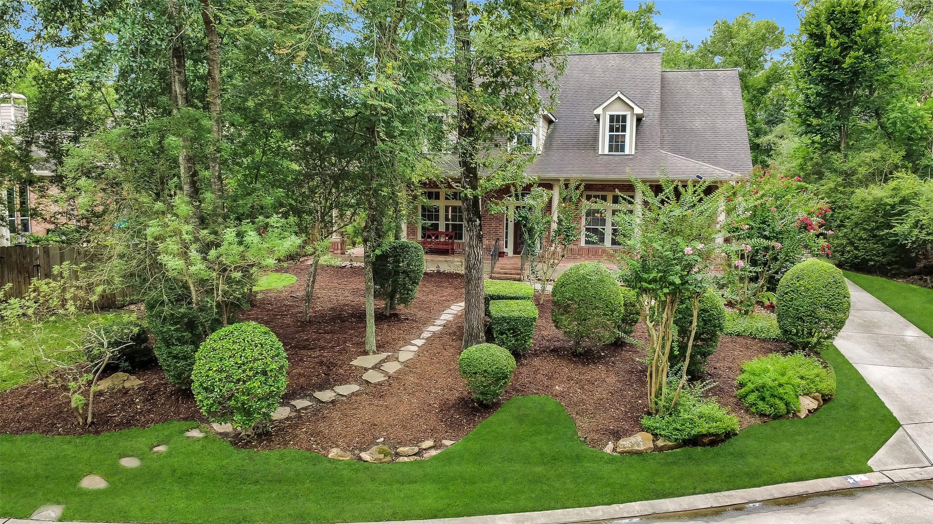7 Larkspur Trail, The Woodlands, TX 77382 Charming two-story home nestled among mature trees, featuring a beautifully landscaped front yard with a stone path leading to a welcoming porch.