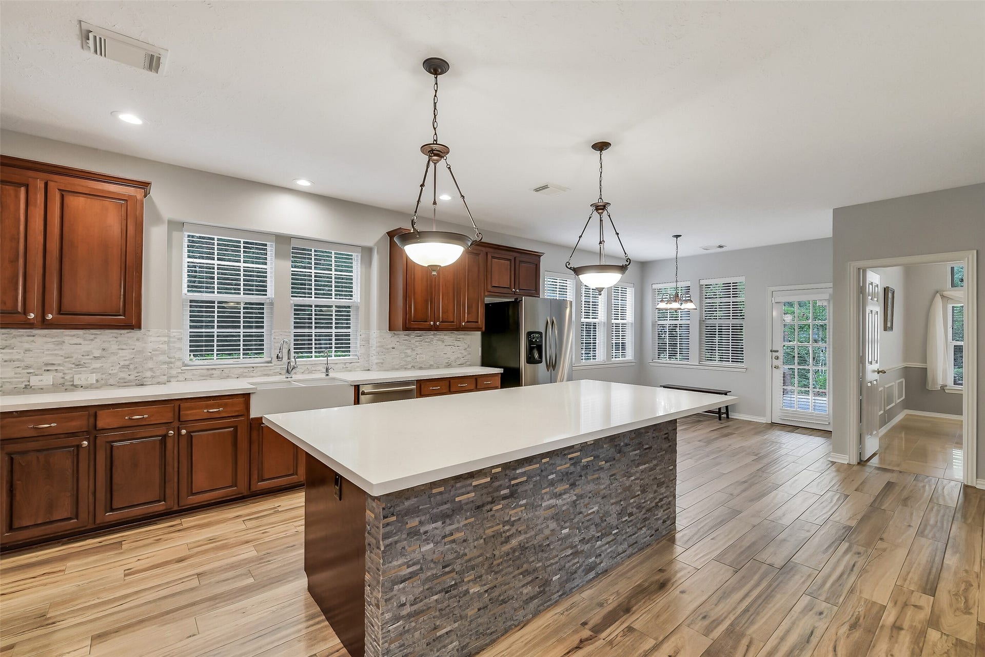 7 Larkspur Trail, The Woodlands, TX 77382 Spacious kitchen with elegant wood cabinetry, a large center island with stone accents, and modern stainless steel appliances. Natural light pours in through multiple windows, highlighting the sleek countertops and open layout.