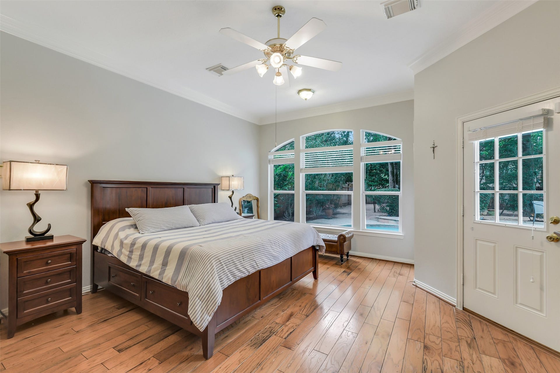 7 Larkspur Trail, The Woodlands, TX 77382 Spacious Primary bedroom with natural light, featuring elegant wood flooring, and a view of the lush backyard through large windows.