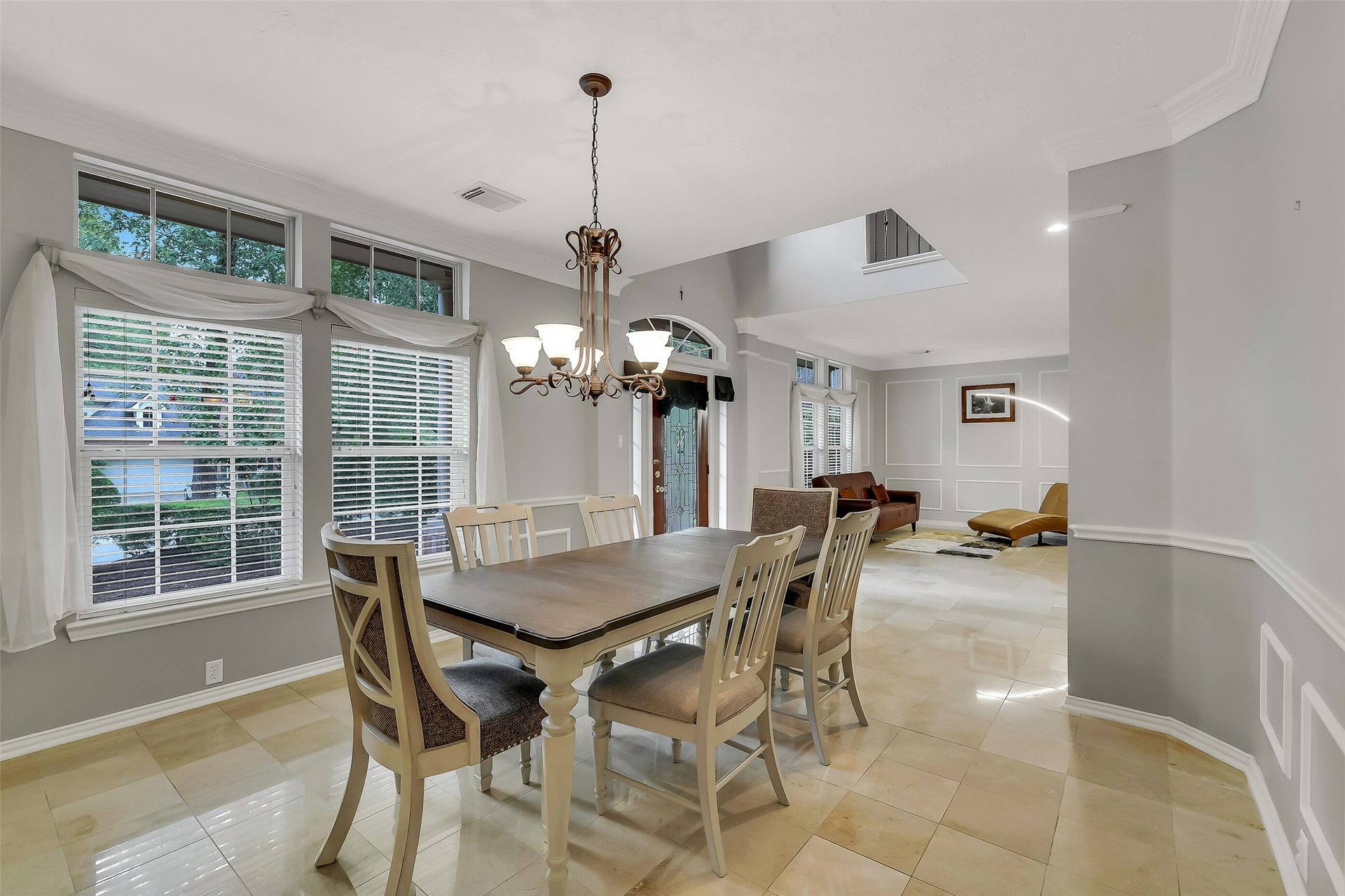 7 Larkspur Trail, The Woodlands, TX 77382 Elegant dining area with large windows, natural light, and a stylish chandelier, seamlessly connecting to a cozy living space with modern decor and marble flooring.