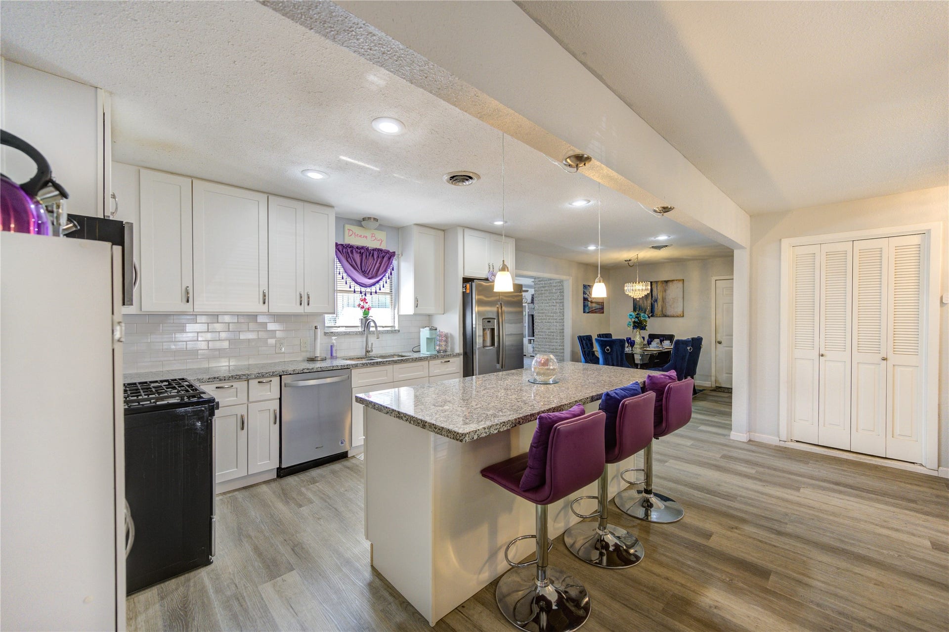 9305 Gettysburg Avenue, Texas City, TX 77591 This spacious kitchen features modern white cabinetry, granite countertops, and a large island with bar seating. The open layout connects to a dining area, complemented by elegant lighting and wood-style flooring. Perfect for entertaining and family gatherings.
