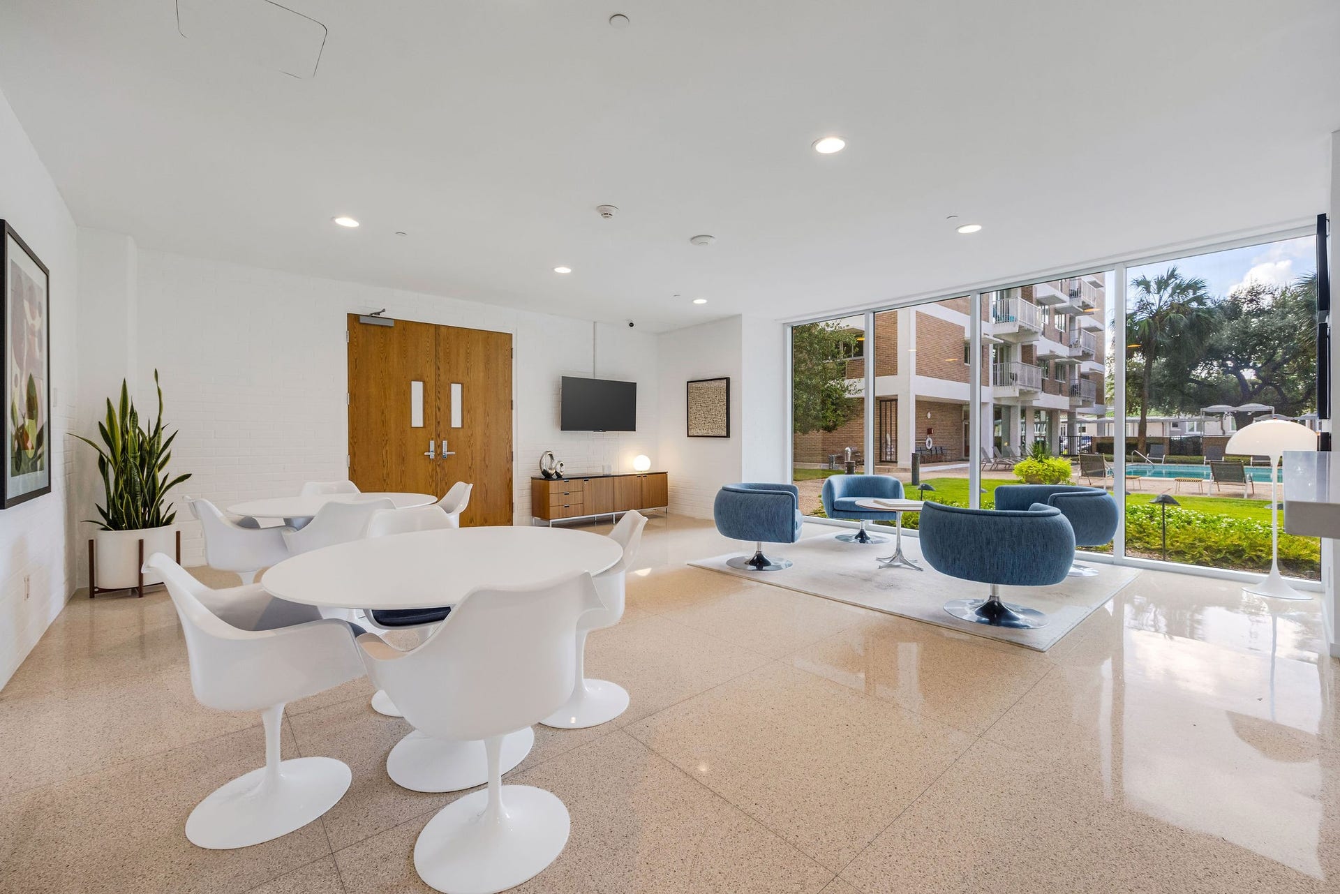 3600 Montrose Boulevard, #501, Houston, TX 77006 Bright and modern communal space featuring sleek white and blue seating, polished floors, and large windows offering views of a lush courtyard and pool area.