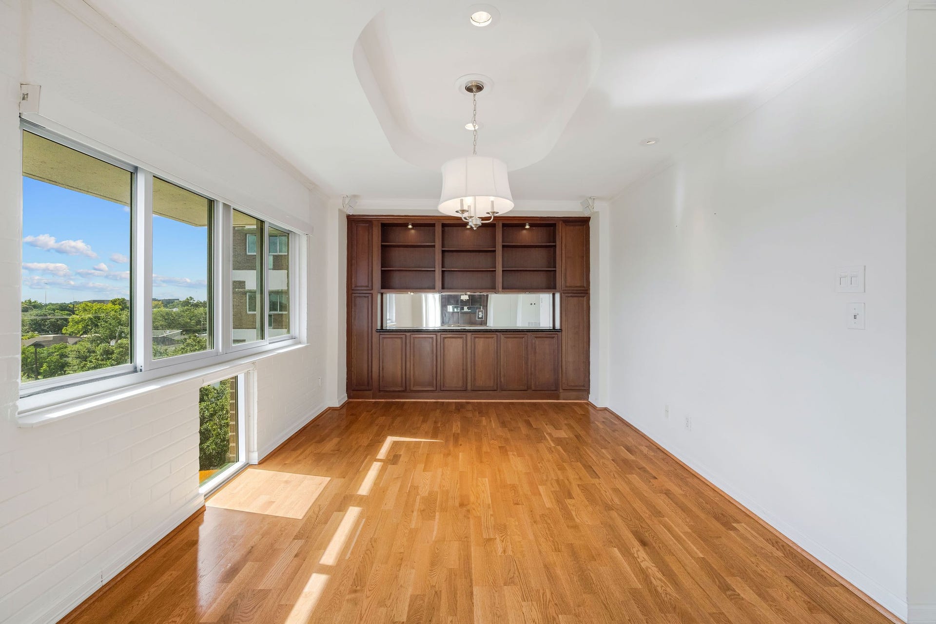 3600 Montrose Boulevard, #501, Houston, TX 77006 Bright and airy room with large windows offering scenic views, complemented by warm hardwood floors and elegant built-in shelving.