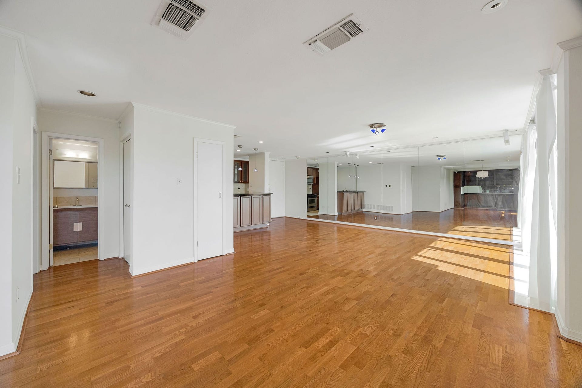 3600 Montrose Boulevard, #501, Houston, TX 77006 Spacious living area with gleaming hardwood floors and abundant natural light, featuring a mirrored wall and open layout that flows into a modern kitchen space.