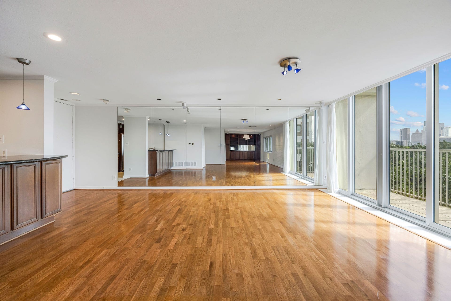 3600 Montrose Boulevard, #501, Houston, TX 77006 Spacious open-concept living area with gleaming hardwood floors, floor-to-ceiling windows offering abundant natural light and stunning city views, complemented by a mirrored accent wall and modern kitchen cabinetry.