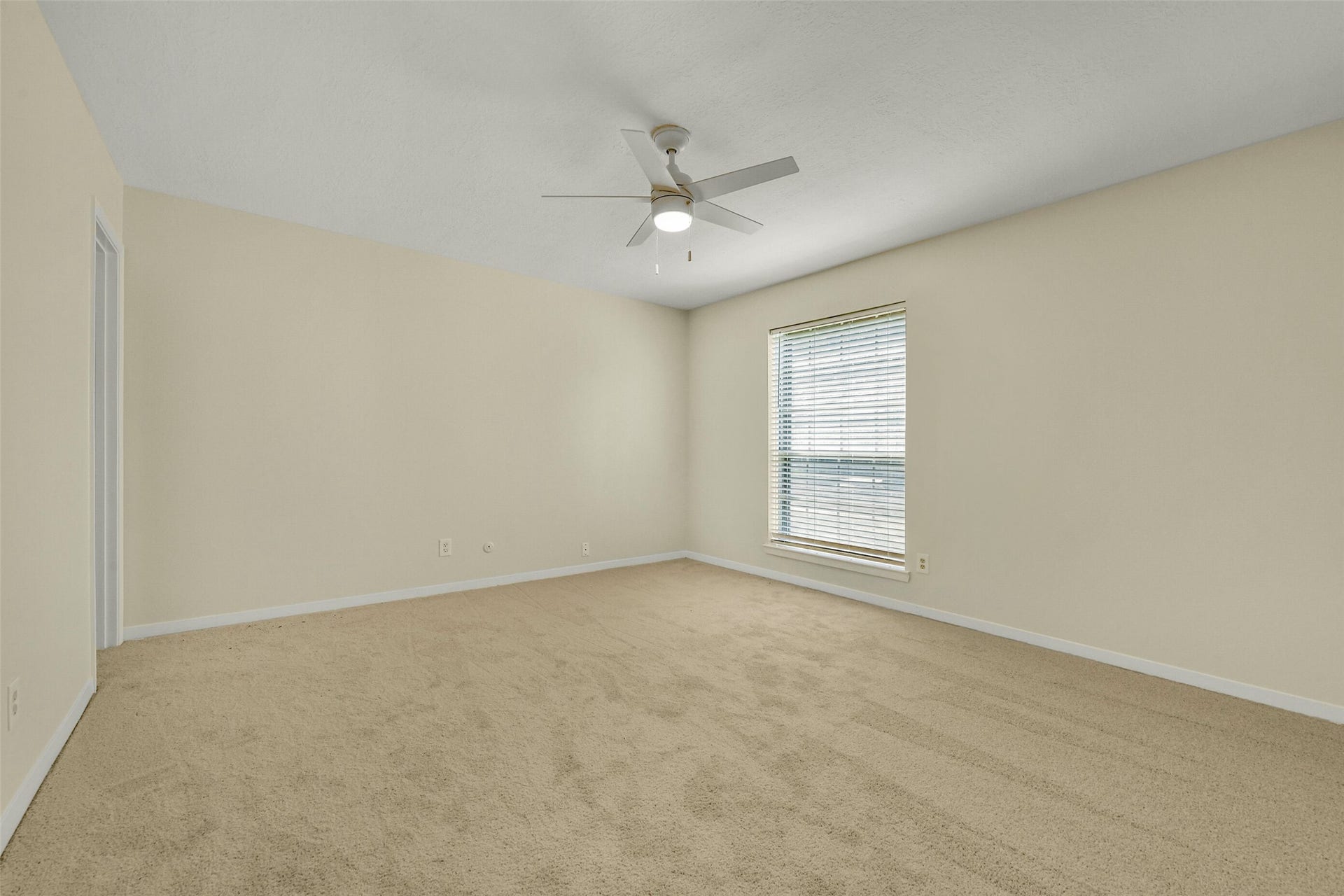 5003 Colombia Drive, Pasadena, TX 77505 Bedroom with soft carpet flooring, neutral walls, and a large window allowing ample natural light, complemented by a modern ceiling fan for comfort.