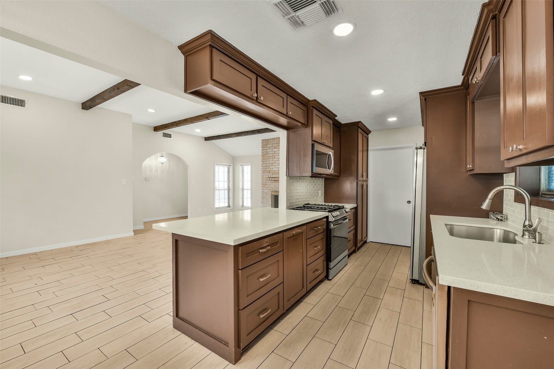 5003 Colombia Drive, Pasadena, TX 77505 Rich wooden cabinetry, modern stainless steel appliances, and sleek countertops, seamlessly opening to a bright living area with stylish wood-look tile flooring and exposed beams.