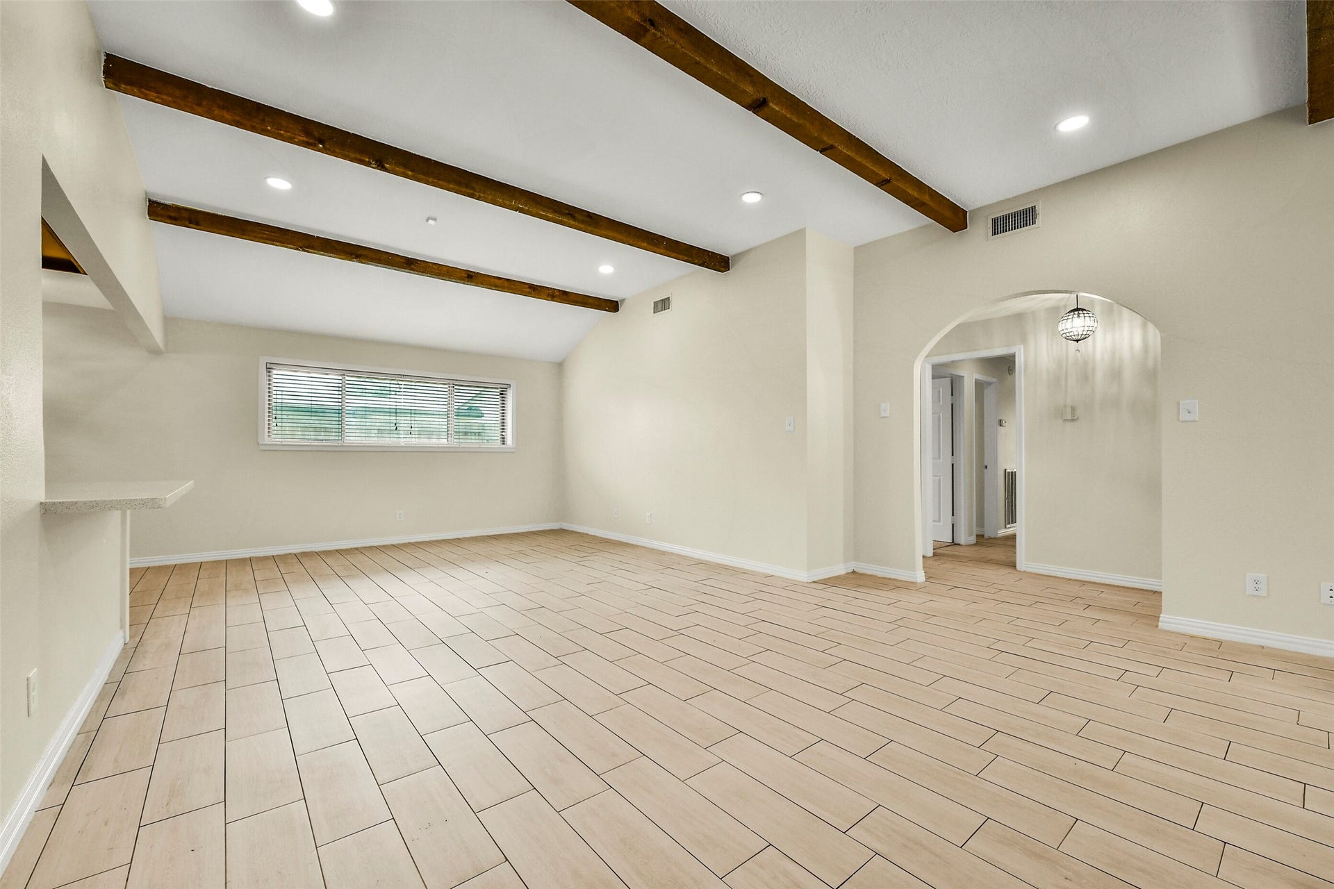 5003 Colombia Drive, Pasadena, TX 77505 Spacious living area with elegant wooden beams, sleek tile flooring, and abundant natural light from a large window, leading into an adjoining room through an arched doorway.