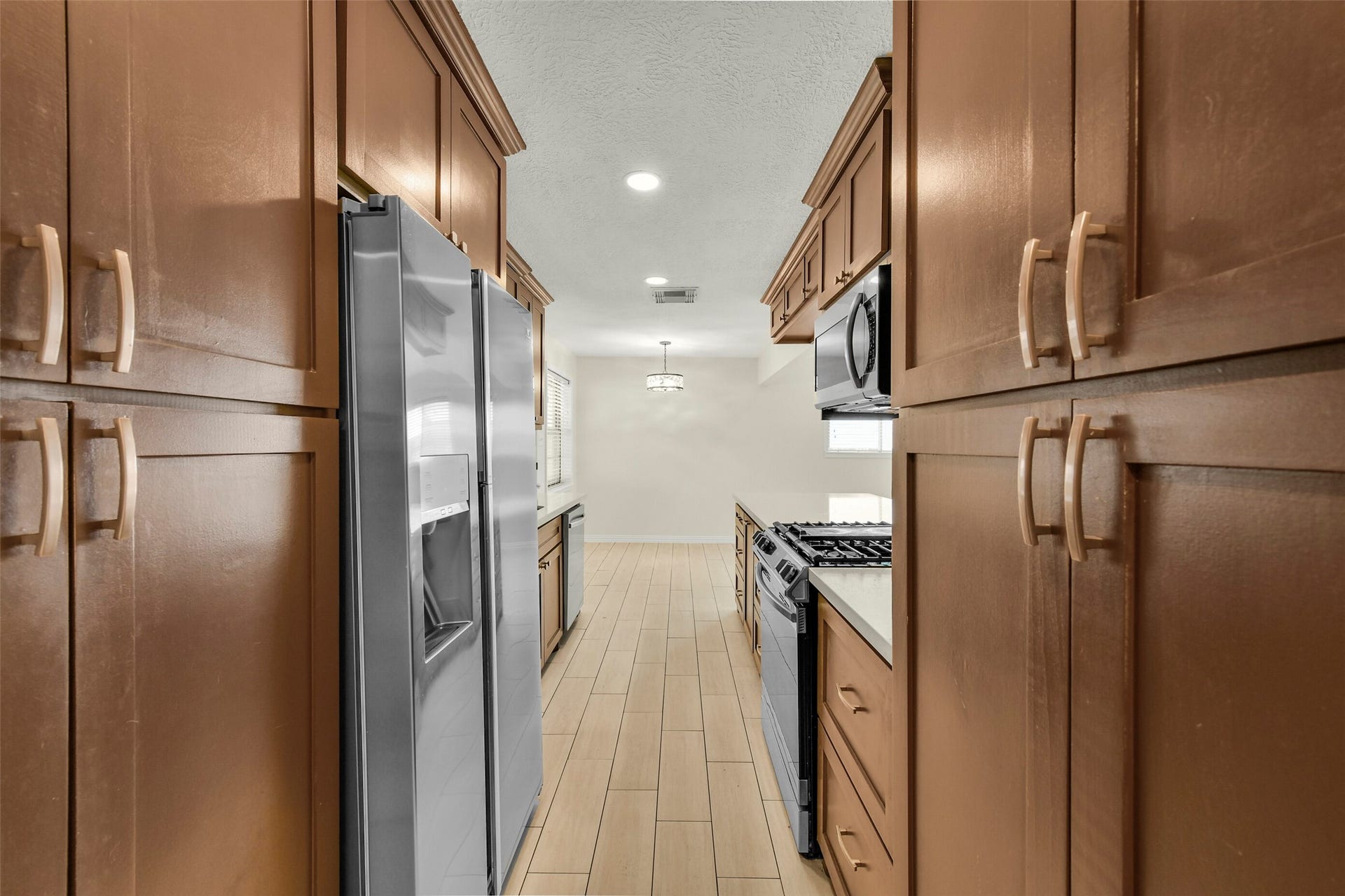 5003 Colombia Drive, Pasadena, TX 77505 Galley kitchen featuring rich wood cabinetry, modern stainless steel appliances, and sleek tile flooring, offering a perfect blend of functionality and elegance.