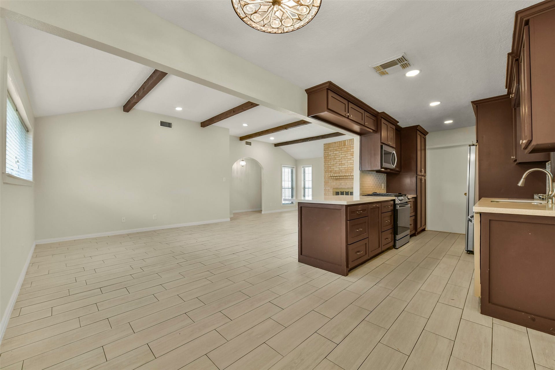 5003 Colombia Drive, Pasadena, TX 77505 Bright, open-concept living space featuring a modern kitchen with rich cabinetry, stainless steel appliances, and elegant wood-beam accents, perfect for entertaining.