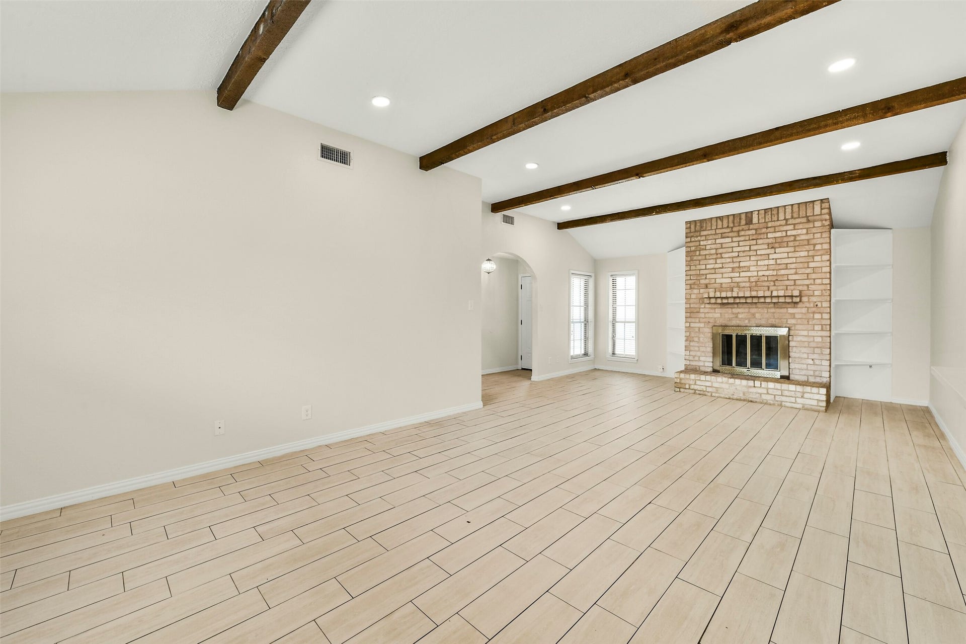 5003 Colombia Drive, Pasadena, TX 77505 Living area featuring elegant wood-look tile flooring, exposed wood beams, and a charming brick fireplace, perfect for cozy gatherings.