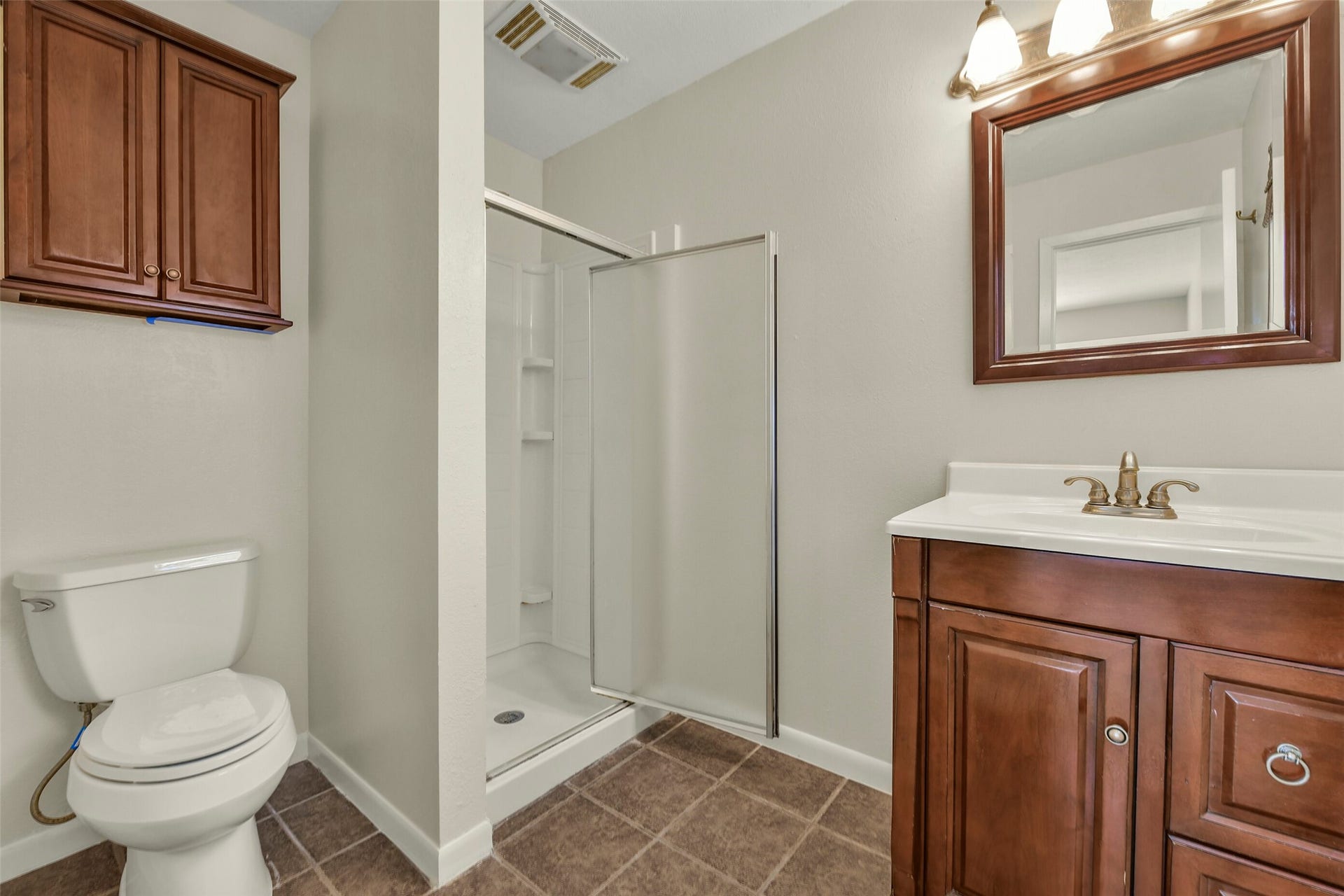 5003 Colombia Drive, Pasadena, TX 77505 Elegant bathroom featuring a glass-enclosed shower, rich wood cabinetry, and a sleek vanity with a matching mirror, offering a blend of functionality and style.