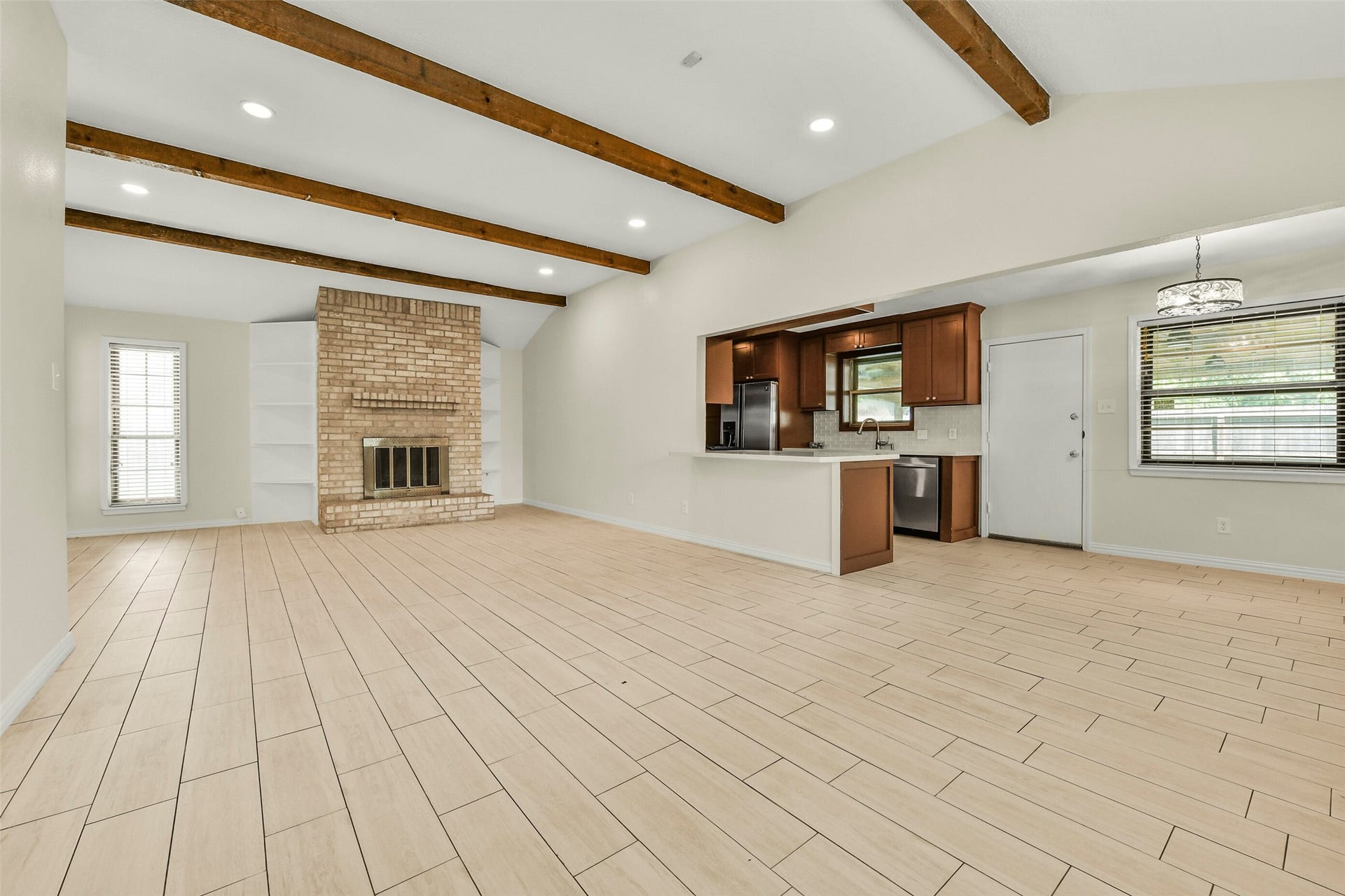 5003 Colombia Drive, Pasadena, TX 77505 Spacious open-concept living area features elegant wood-beam ceilings, a cozy brick fireplace, and sleek tile flooring, seamlessly connecting to a modern kitchen with stainless steel appliances and warm cabinetry.
