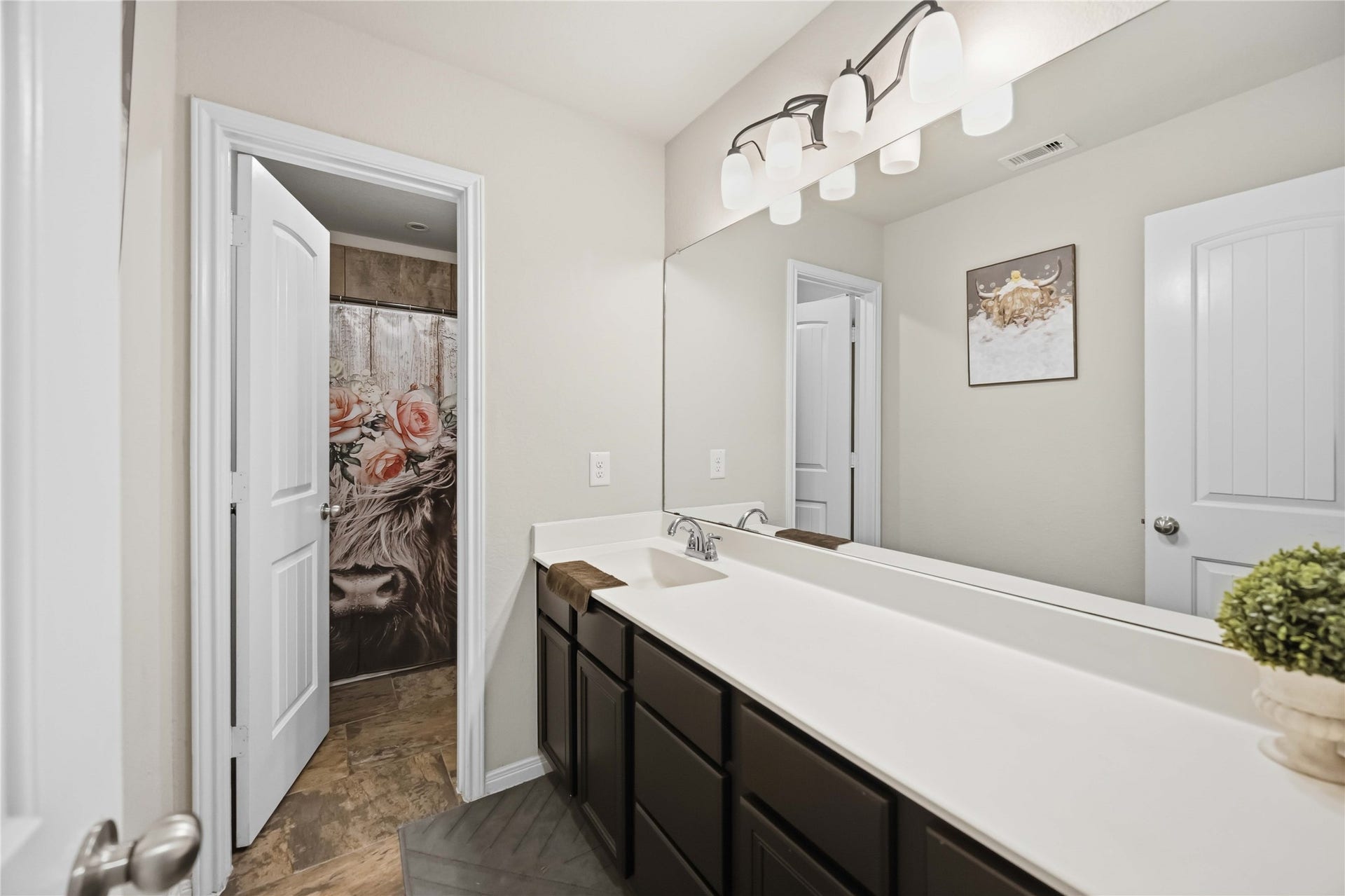 712 Rim Water Drive, Alvin, TX 77511 Bright and modern bathroom featuring a sleek vanity with ample storage, contemporary lighting, and a decorative shower curtain adding a touch of elegance.