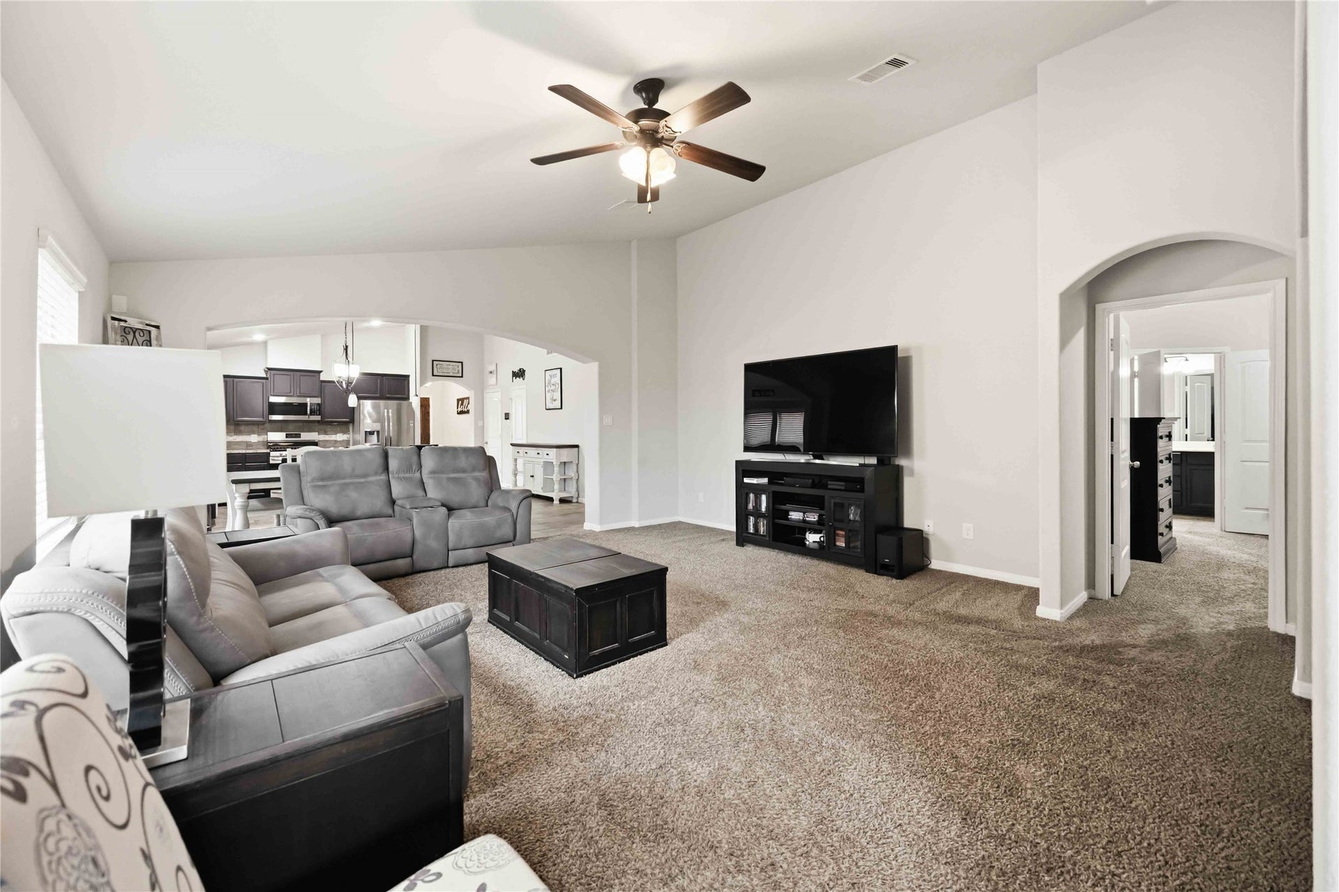 712 Rim Water Drive, Alvin, TX 77511 Spacious living room with plush carpeting, a ceiling fan, and modern furnishings, seamlessly connected to an open-concept kitchen and dining area.