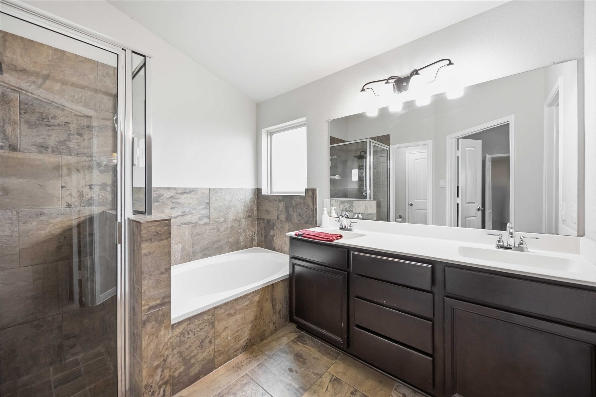 712 Rim Water Drive, Alvin, TX 77511 Primary bathroom featuring a luxurious soaking tub, separate glass-enclosed shower, and dual sinks with elegant dark cabinetry for ample storage.