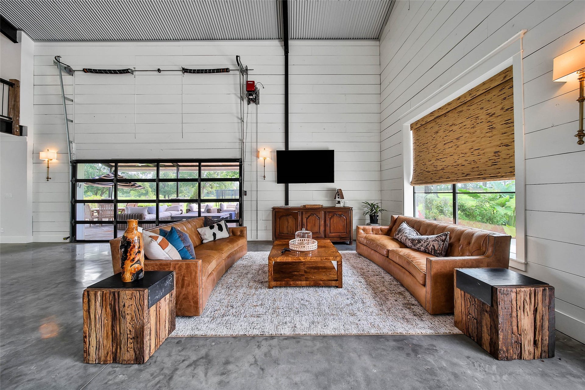 Inviting living area with soaring 20-foot metal ceilings, expansive remote-controlled glass bay doors, abundant natural light, and seamless access to the covered outdoor living spacedesigned for effortless indoor-outdoor entertaining.