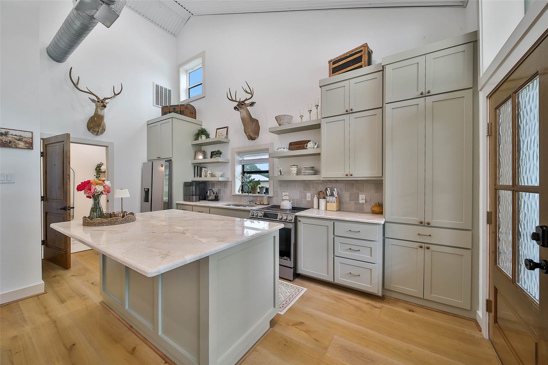 Private garage apartment kitchen showcases Taj Mahal quartzite countertops, custom-painted cabinetry, oversized island, soaring ceilings and beautiful 10" real wood plank floors.