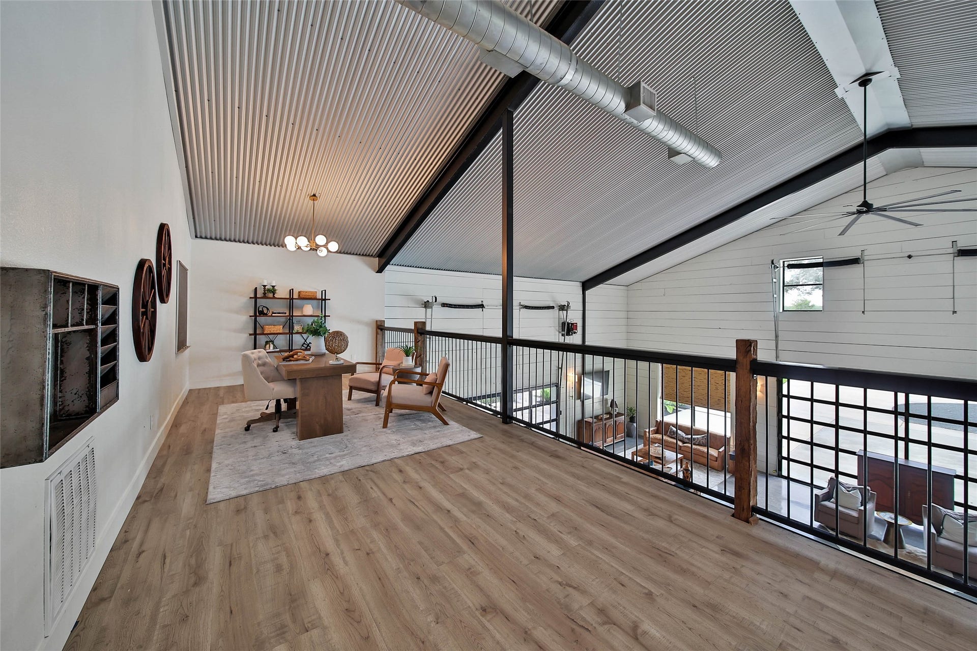 Open loft-style home office overlooking the great room, corrugated metal ceiling, exposed ductwork, custom iron railing with reclaimed 200-year-old barn wood accents, designer lighting, and an inspiring workspace with expansive views below.