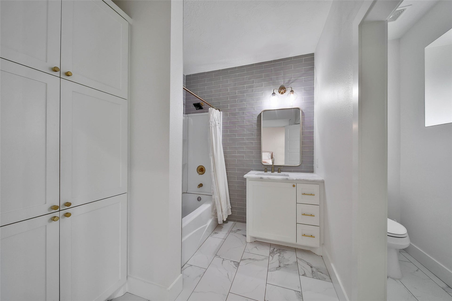 Well-appointed upstairs bathroom with marble-look tile flooring, linen storage and tiled tub/shower combination.