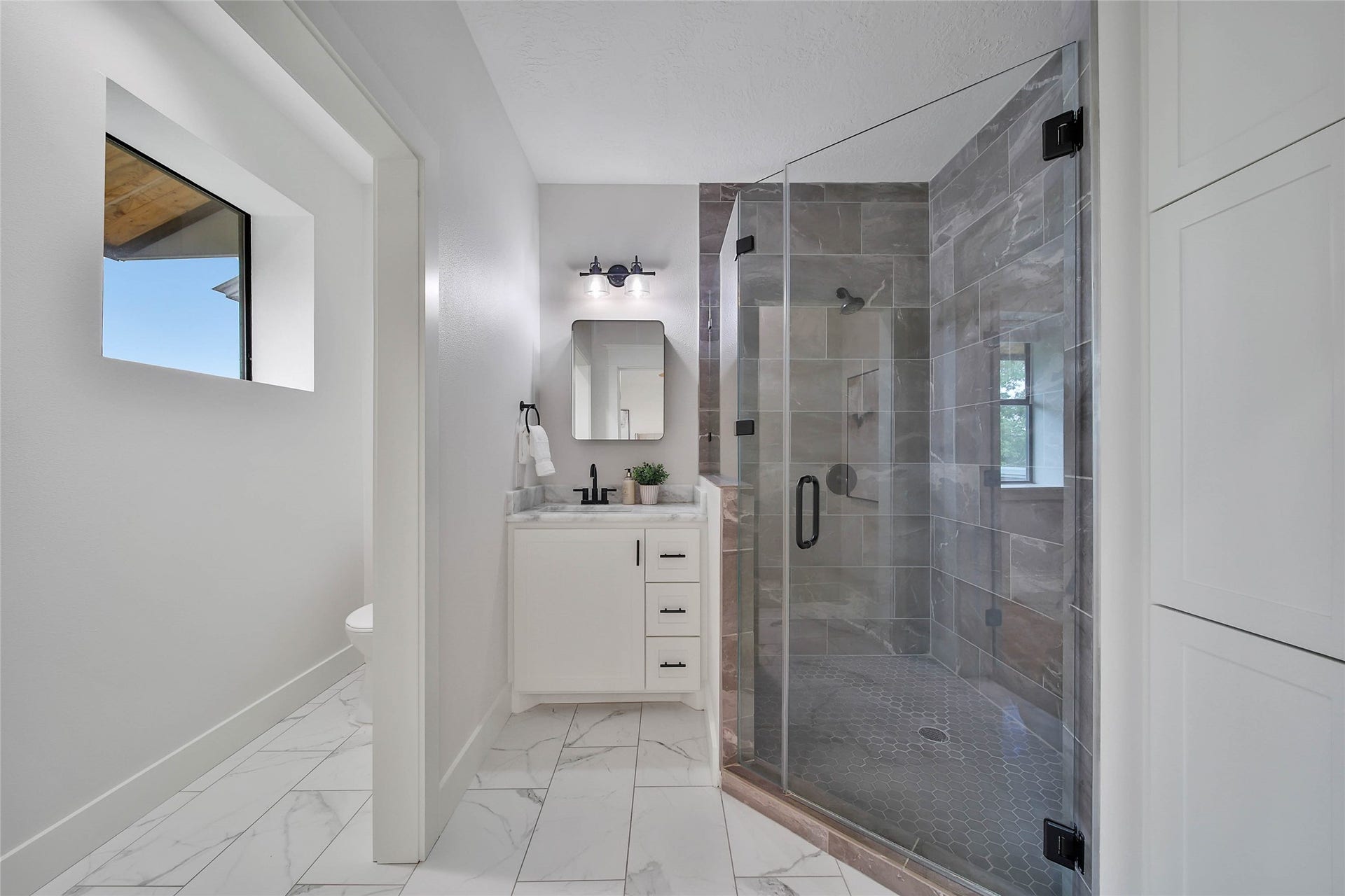 Stylish upstairs bathroom featuring a walk-in frameless glass shower with designer tile, black fixtures, marble-look flooring, and storage.