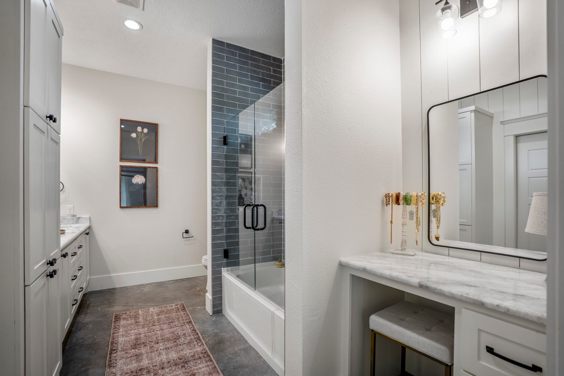 Spa-inspired primary bath featuring dual vanities, built-in vanity, custom cabinetry, concrete floors, linen storage, and a beautifully tiled tub/shower combination with sleek frameless glass enclosure.