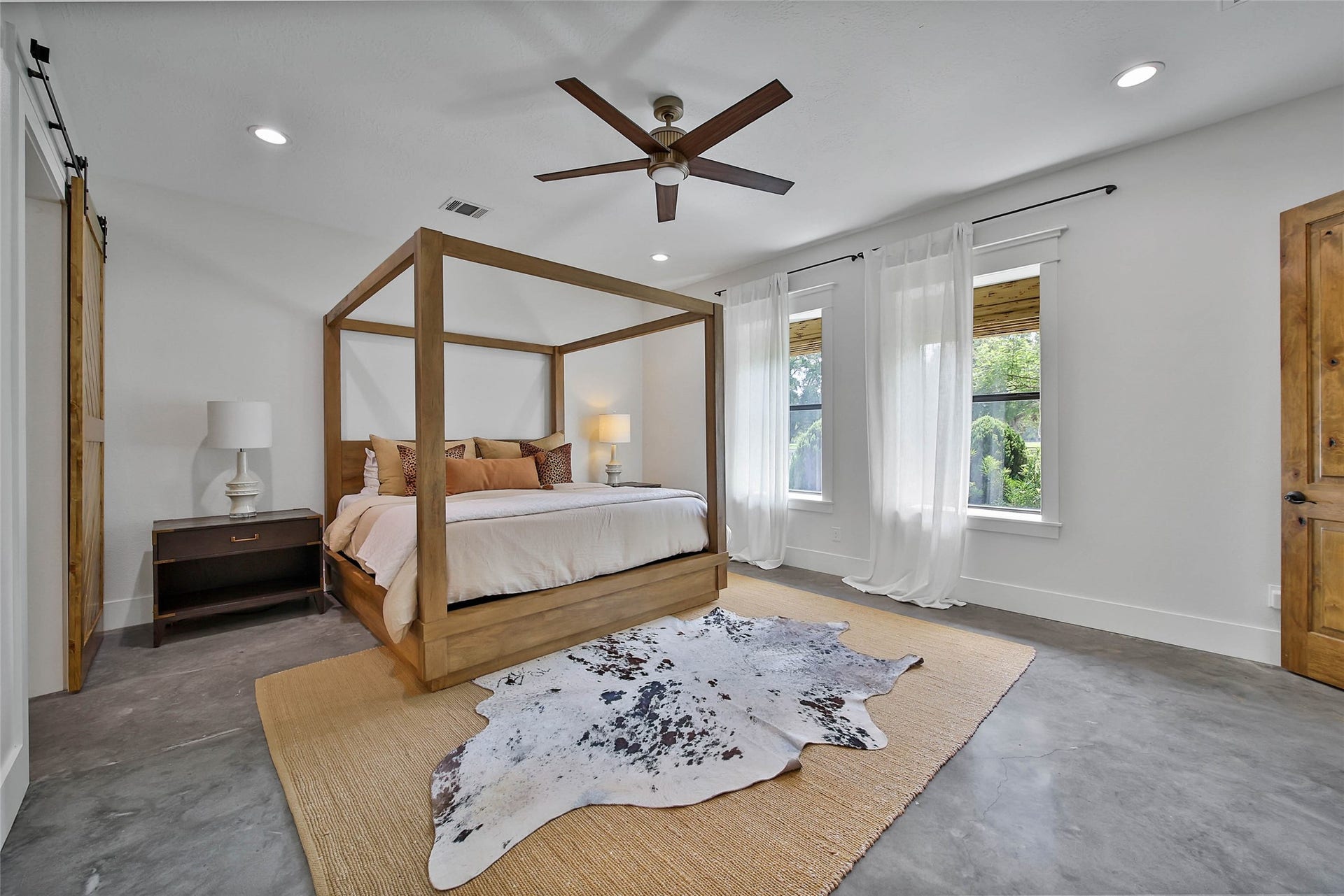 Spacious primary suite offering concrete floors, oversized windows with serene property views, sliding barn door into ensuite bath.