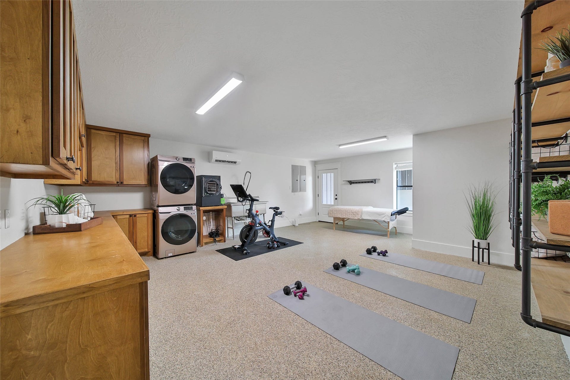 Versatile flex room ideal for a home gym, hobby space, office, or studio, featuring durable epoxy flooring, built-in cabinetry with utility sink, additional washer/dryer hookups, mini-split HVAC, and direct exterior access. Home offers two laundry areas, including a dedicated laundry room plus this secondary laundry station for added convenience.