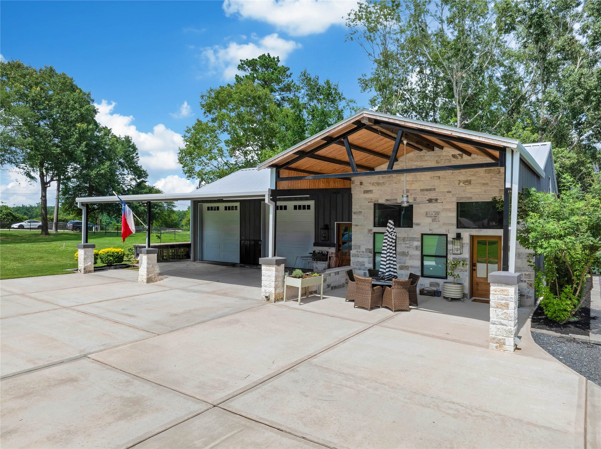 Detached 35x17 party garage with two 10' insulated garage doors, adjoining private 700 sq ft apartment, tongue-and-groove wood ceiling with exposed steel beams and Big Ass Fan, and covered porch accented by stone and stucco columns.